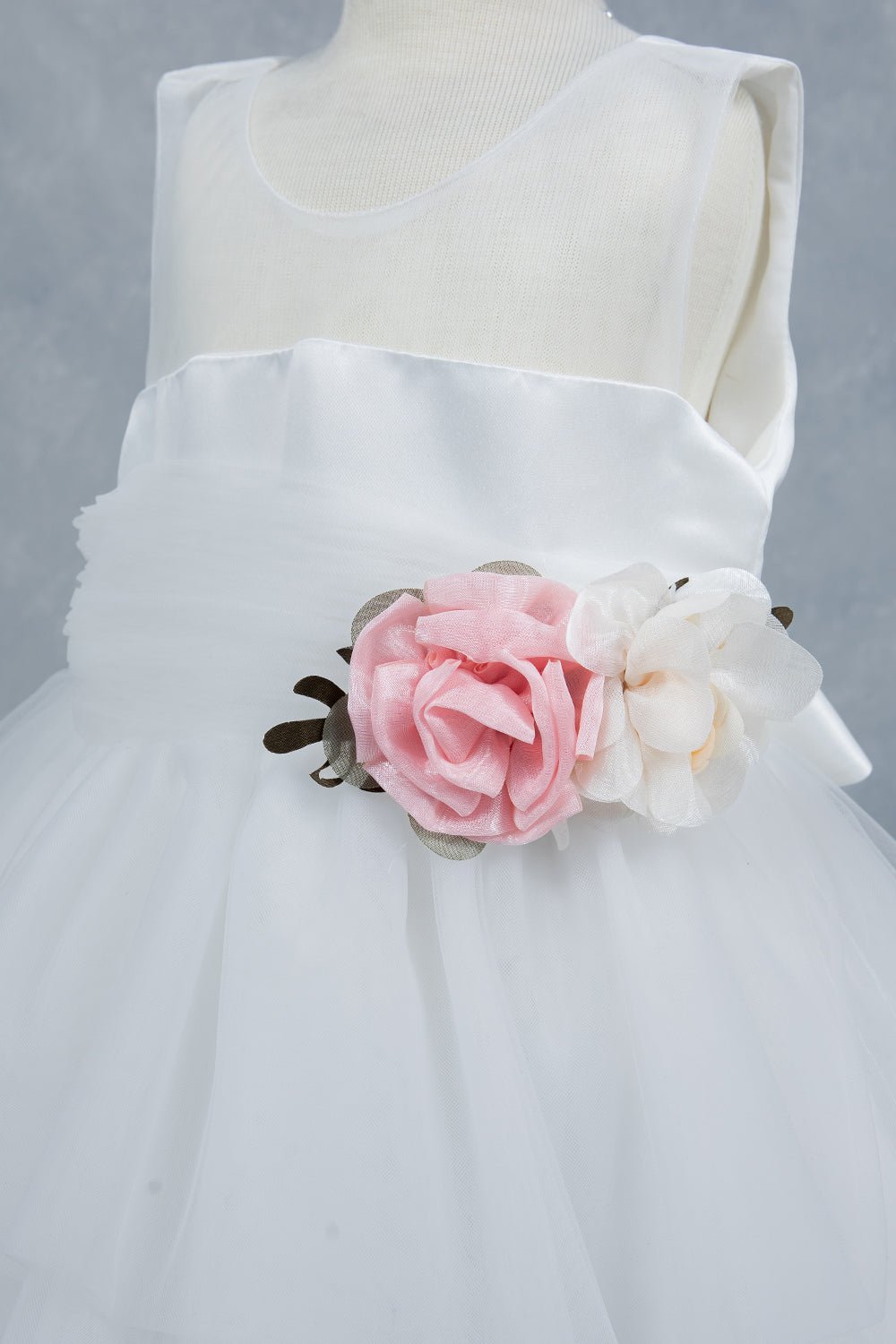 Close-up front view of white flower girl dress showing floral embellishment and satin waistband.