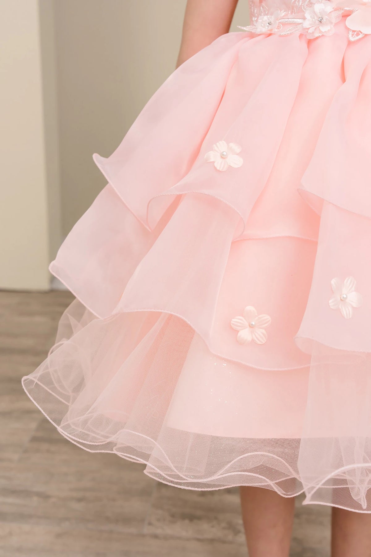 Close-up of a peach blush flower girl dress with ruffled layers and floral details.