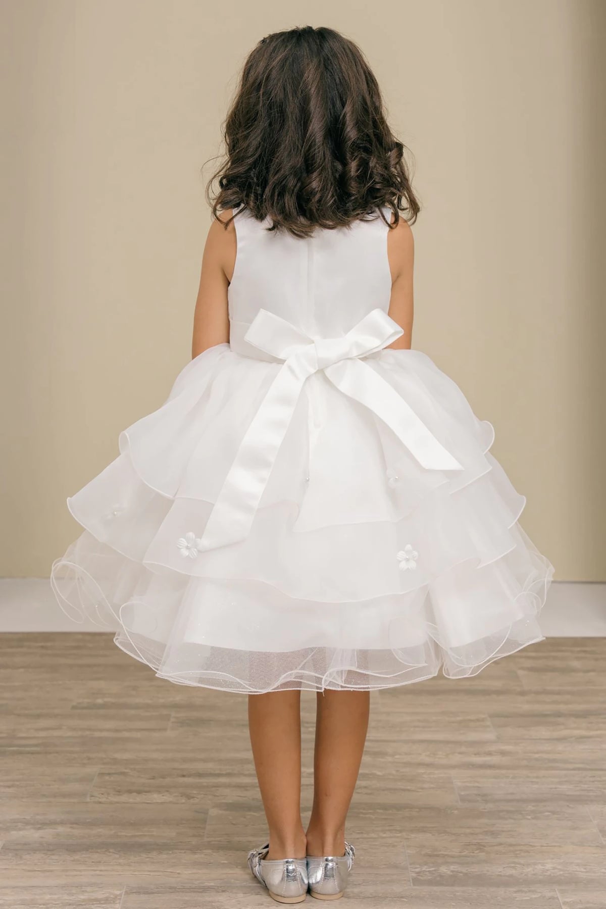 A white flower girl dress with a large bow at the back.