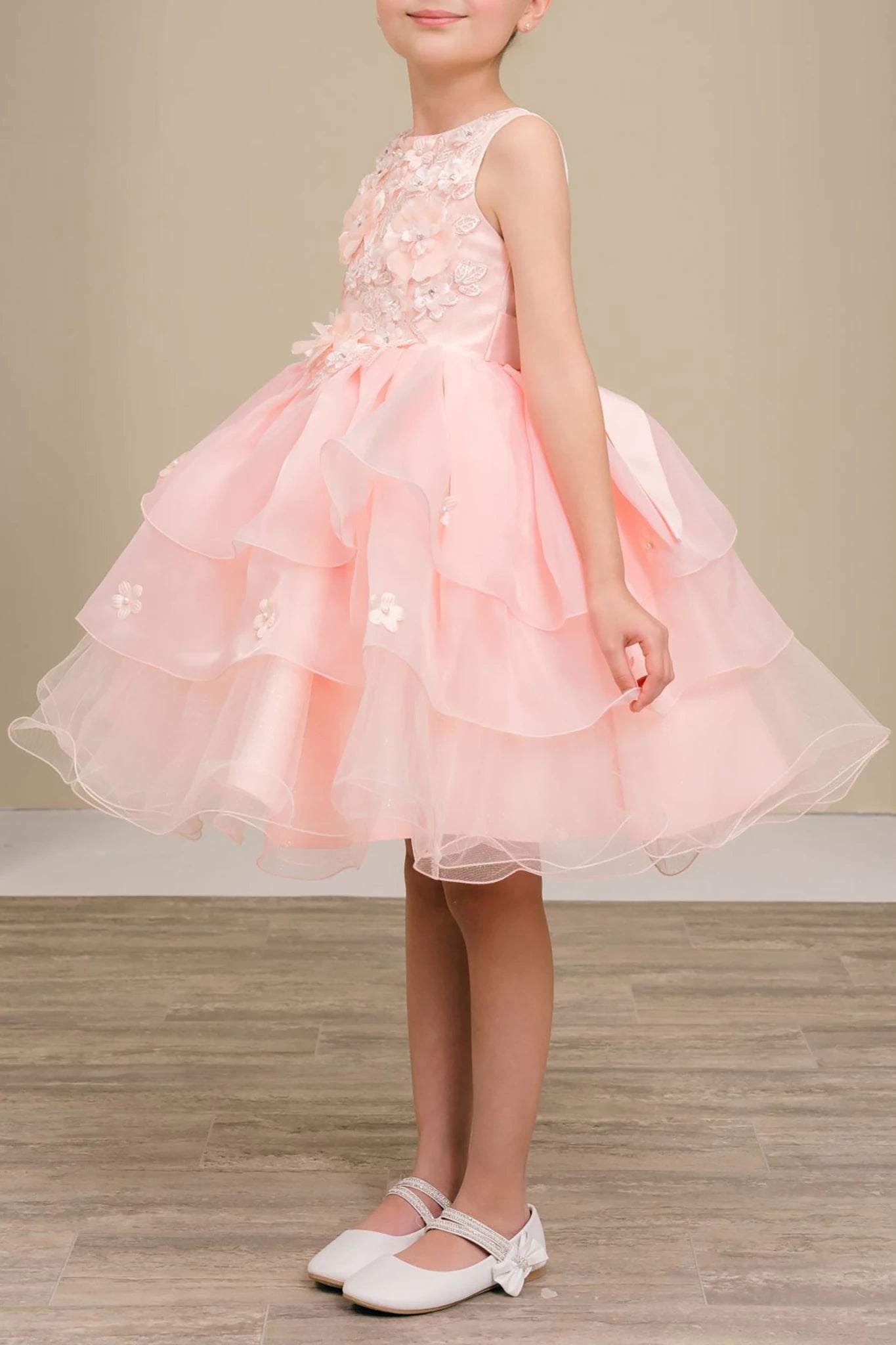 Young girl wearing a peach blush dress with floral details on a wooden floor.