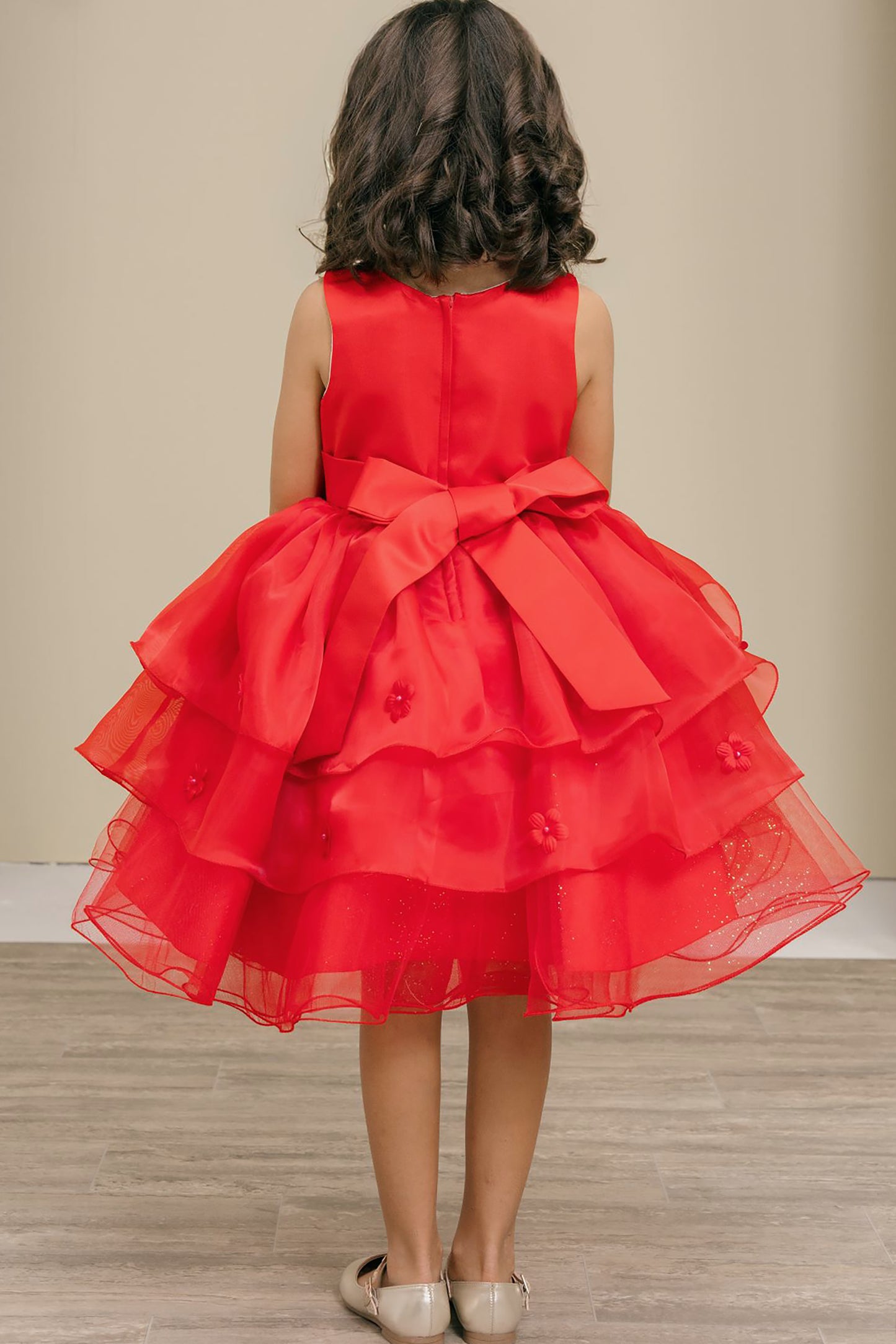 Red dress with a large bow on the back worn by a child, standing against a neutral background.