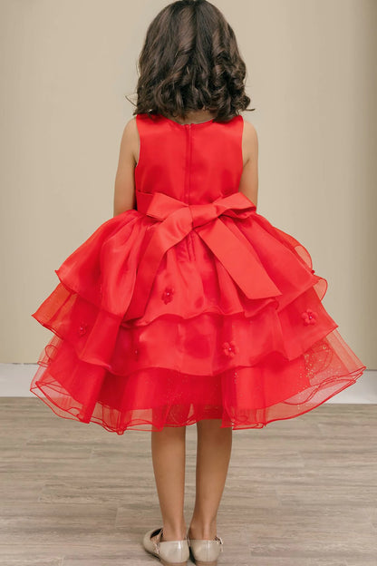 Red dress with a large bow on the back worn by a child, standing against a neutral background.