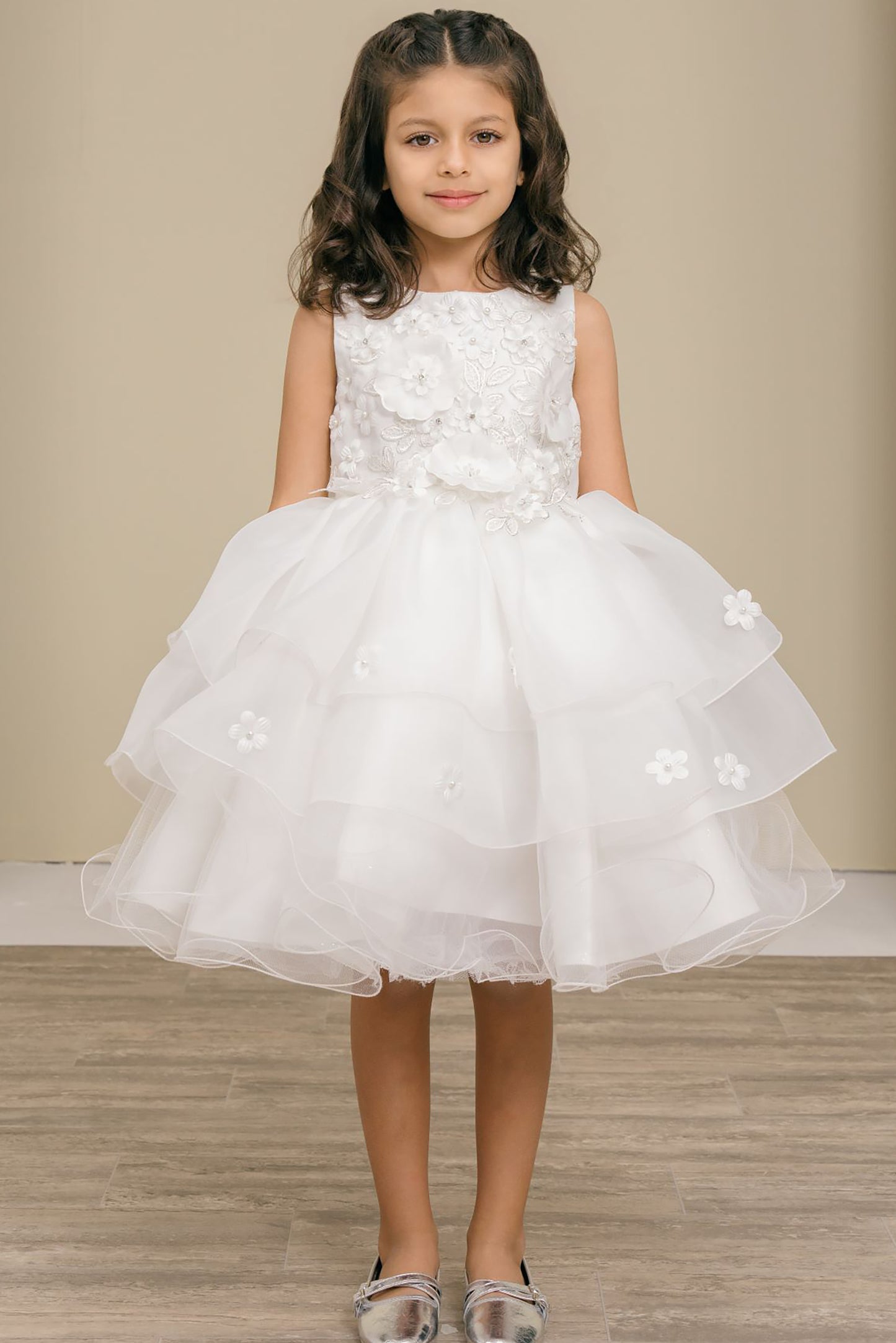 Young girl wearing a white floral dress against a beige wall.