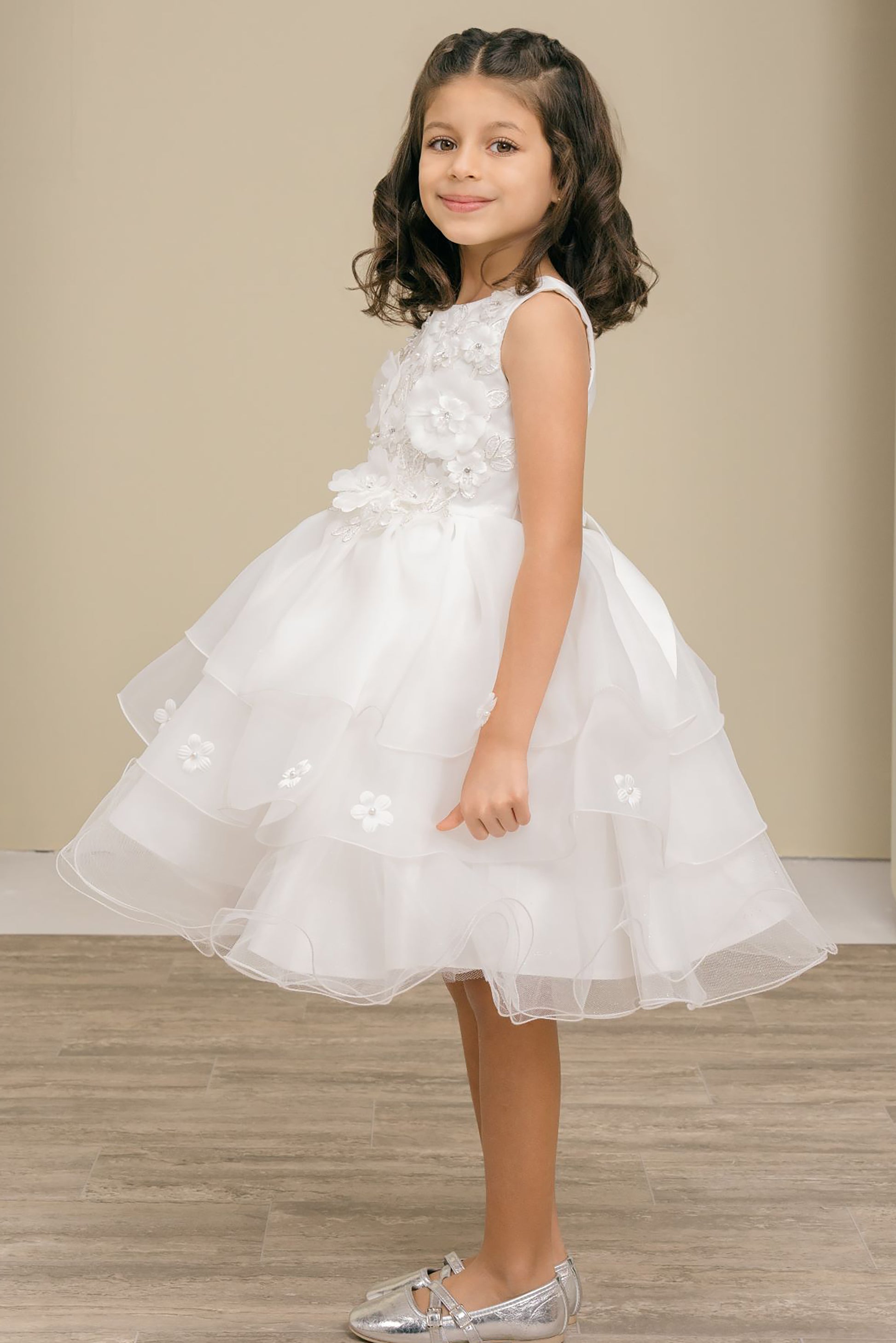 Young girl wearing a white floral dress on a wooden floor with a beige wall background