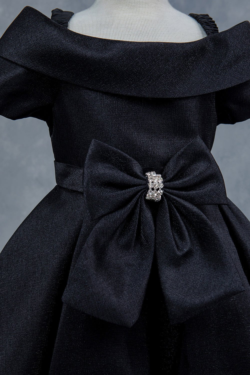 Close-up front view of black dress showing rhinestone bow detail and collar