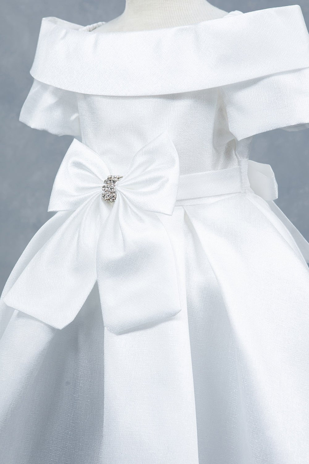 Close-up front view of white dress showing rhinestone bow detail and collar