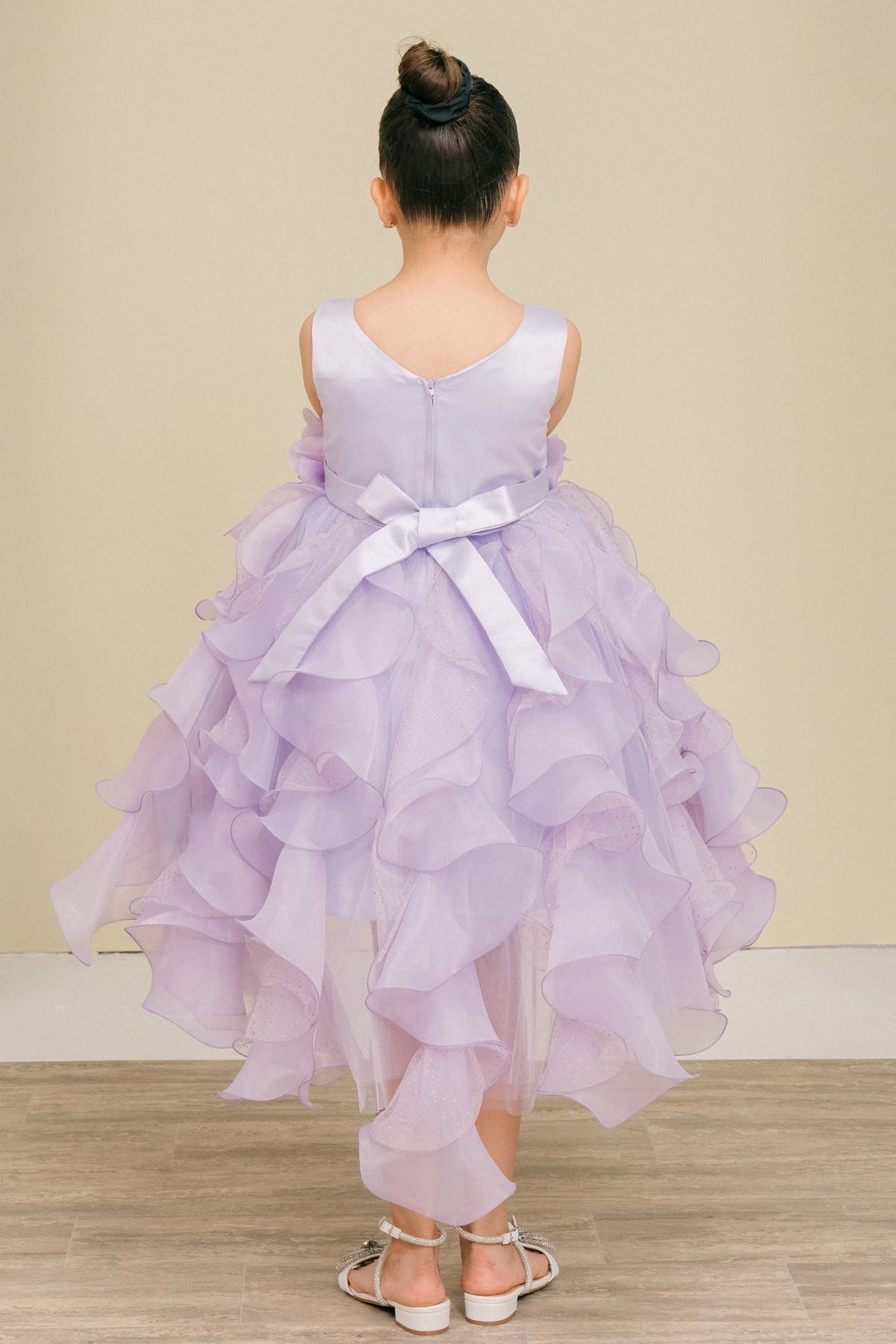 Showcasing with a bow above petal-shaped ruffles, this Lilac kids party dress displays elegant detail.