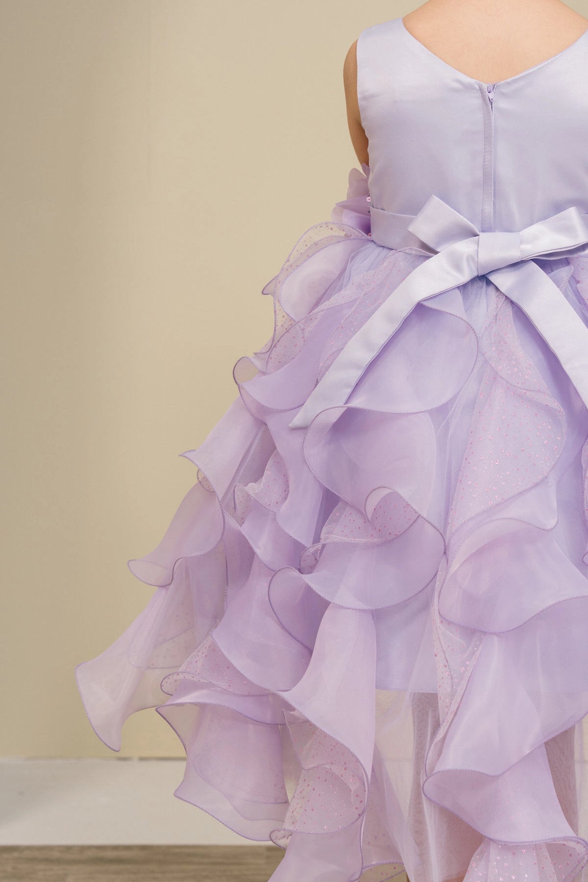Finished details of a bow above petal-shaped ruffles distinguish the Lilac kids party dress.