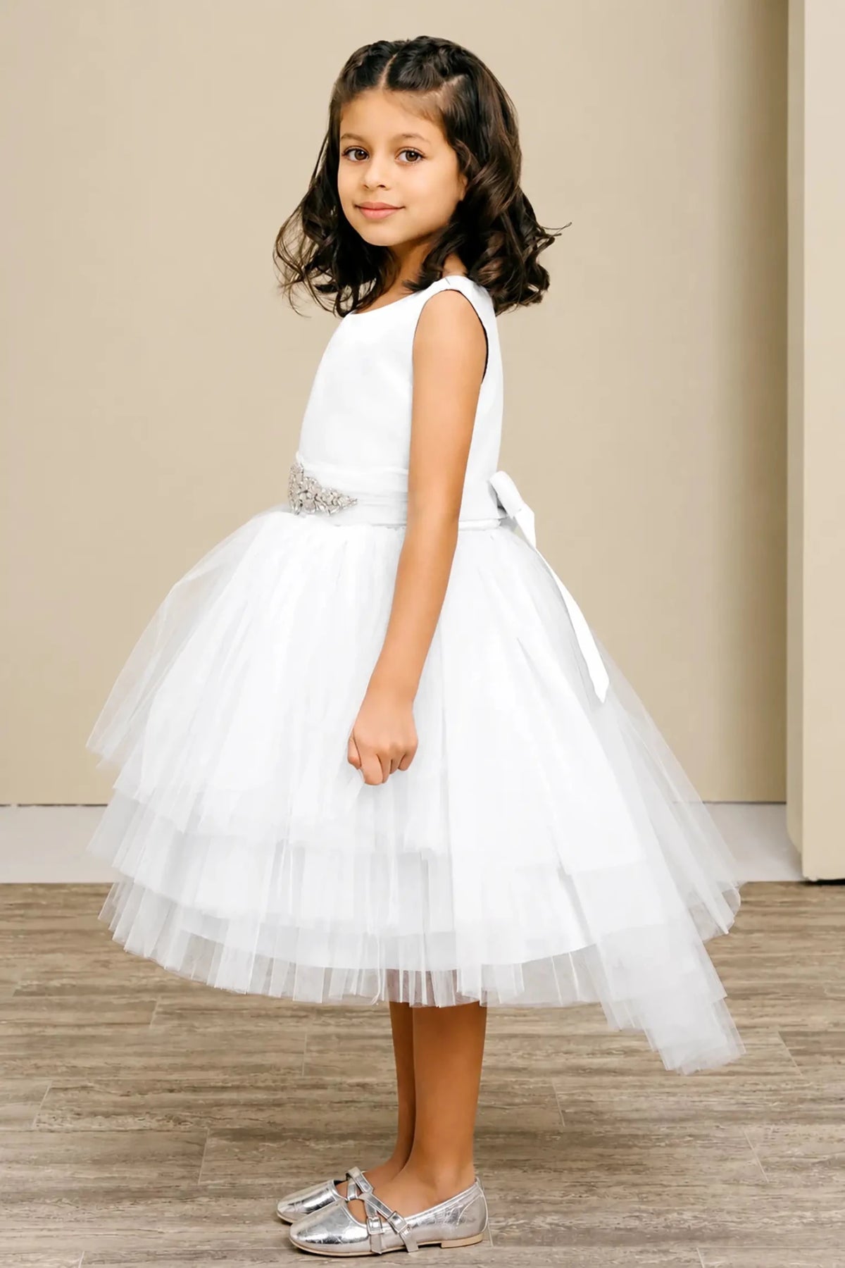 White flower girl dress with satin bodice, rhinestone waistband, satin bow back, and layered tulle skirt.