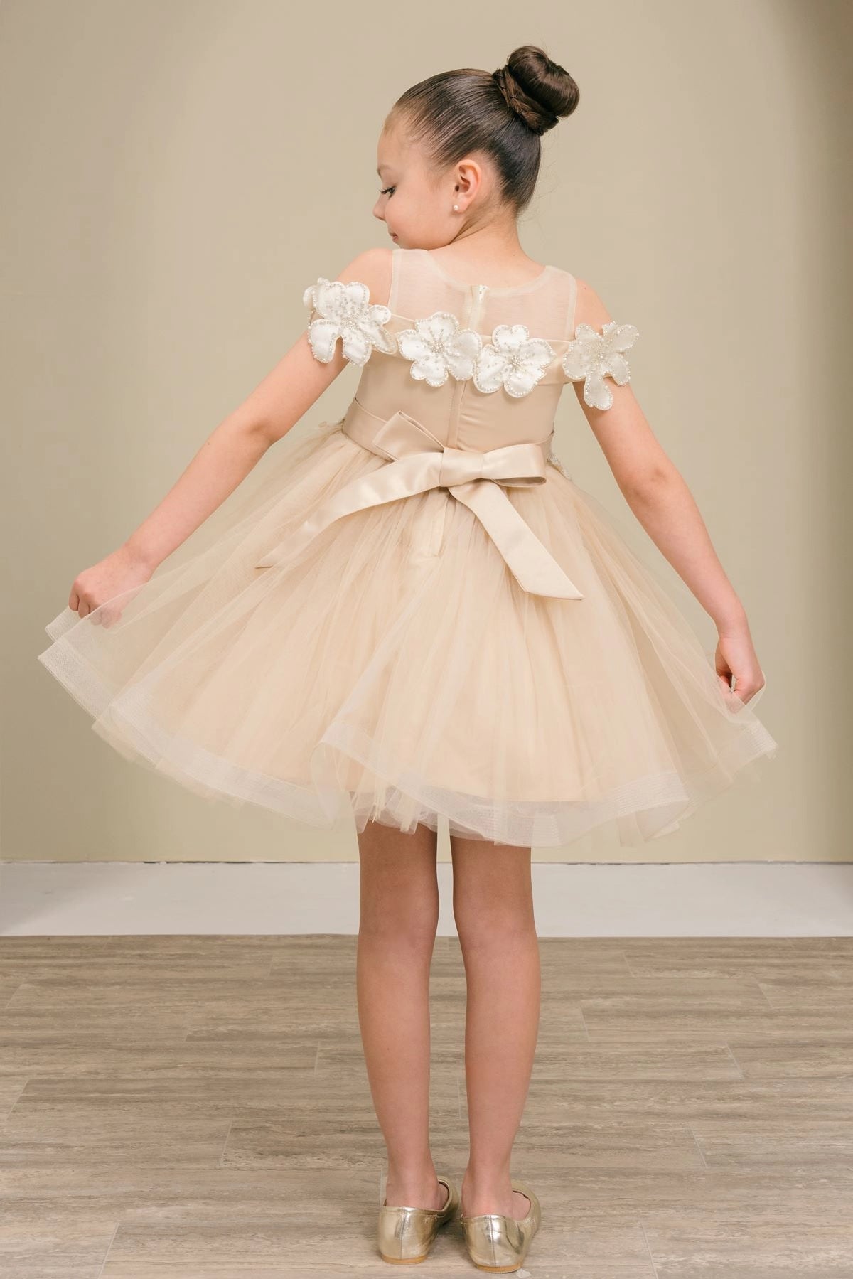 A Champagne flower girl dress showing back sash bow beneath the floral shoulder trim.