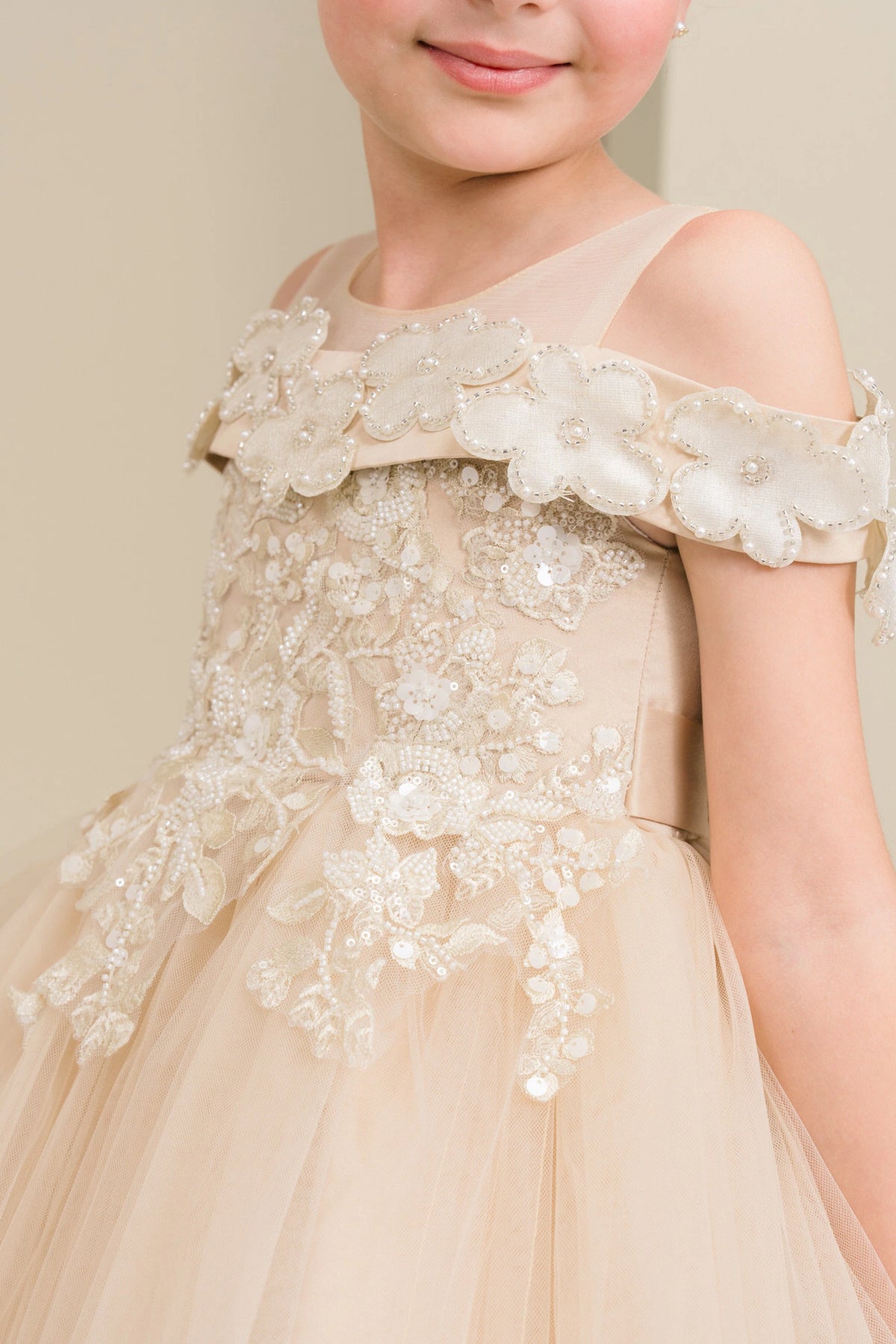 Details of the Champagne flower girl dress include dimensional flowers around the off-shoulder trim.