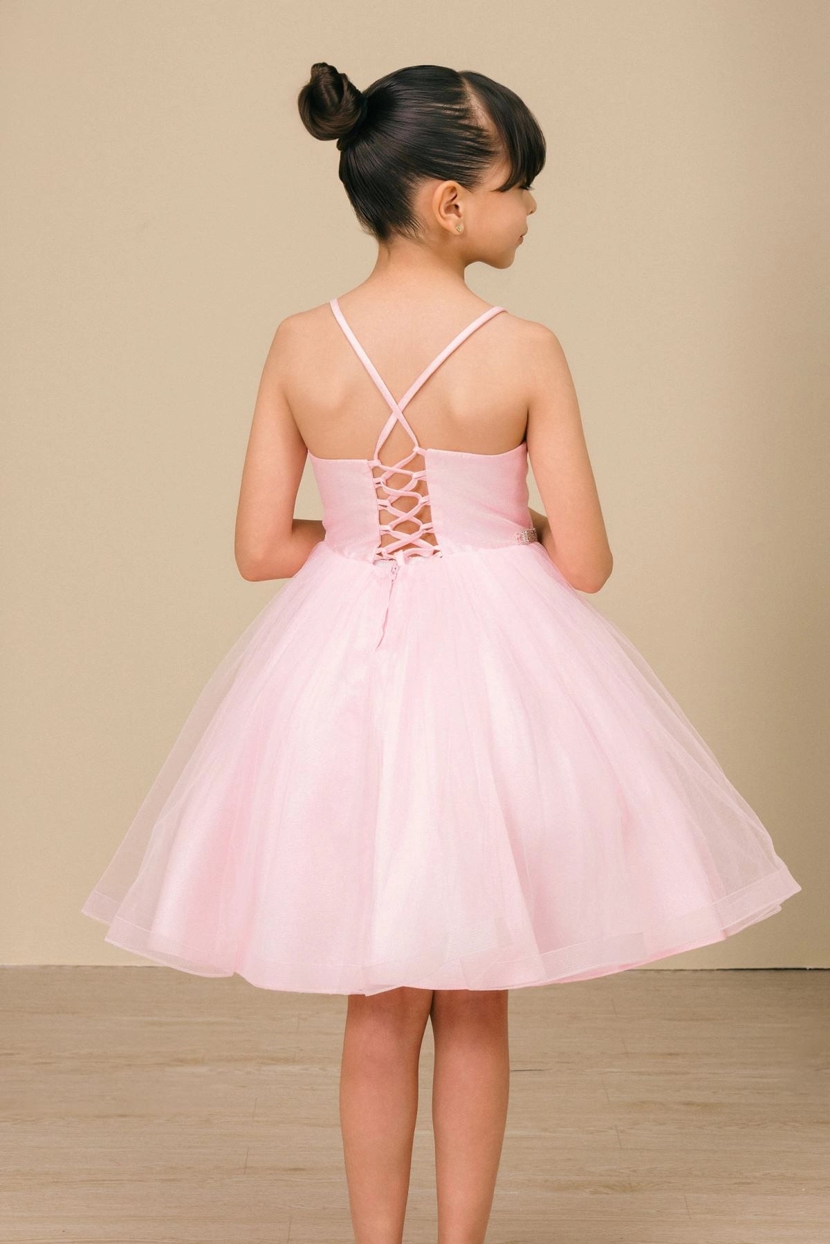 A Pink flower girl dress showing crossed straps and lace-up back.
