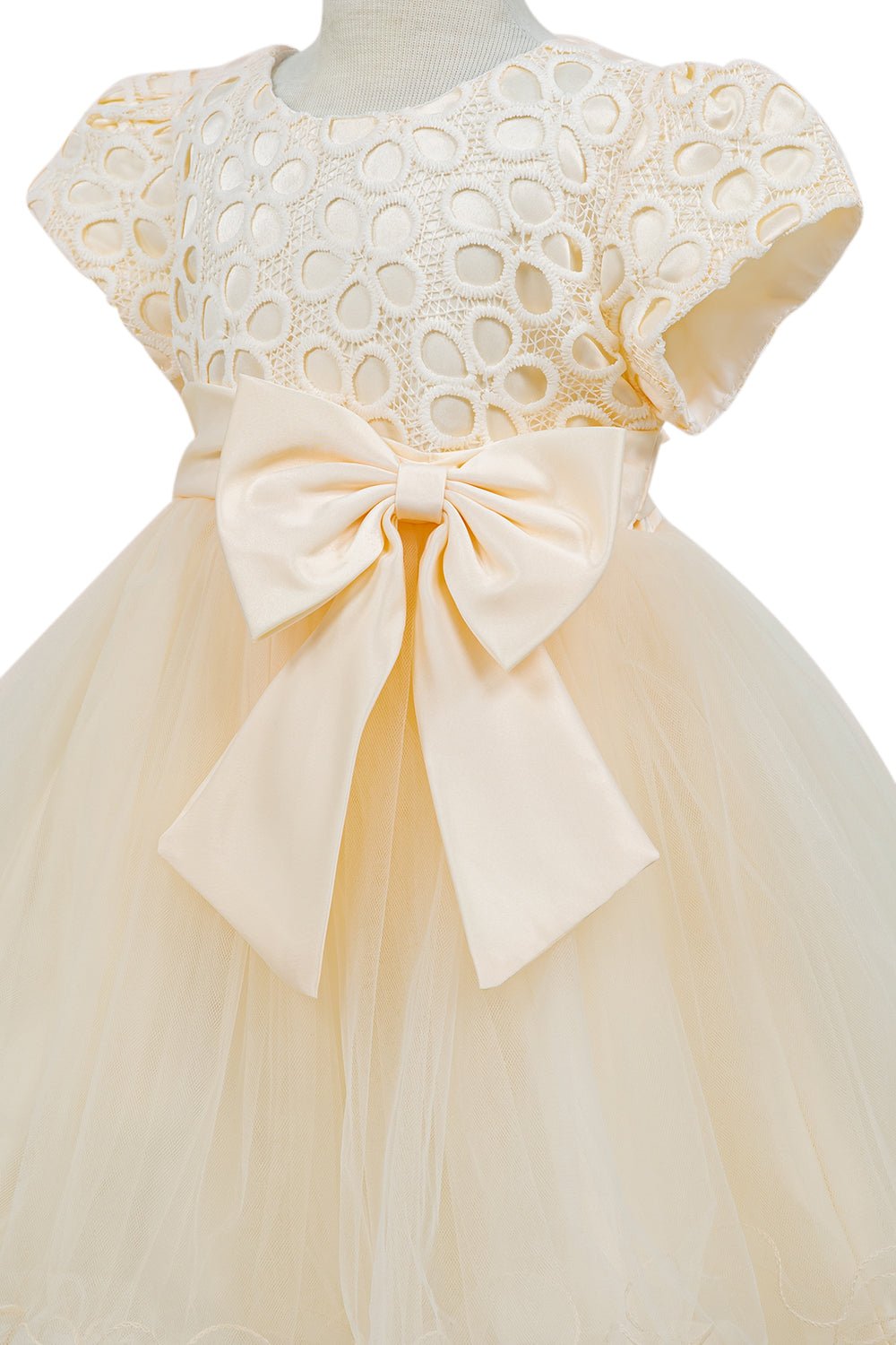 Close-up front view of champagne flower girl dress showing lace detail satin sash and oversized bow.
