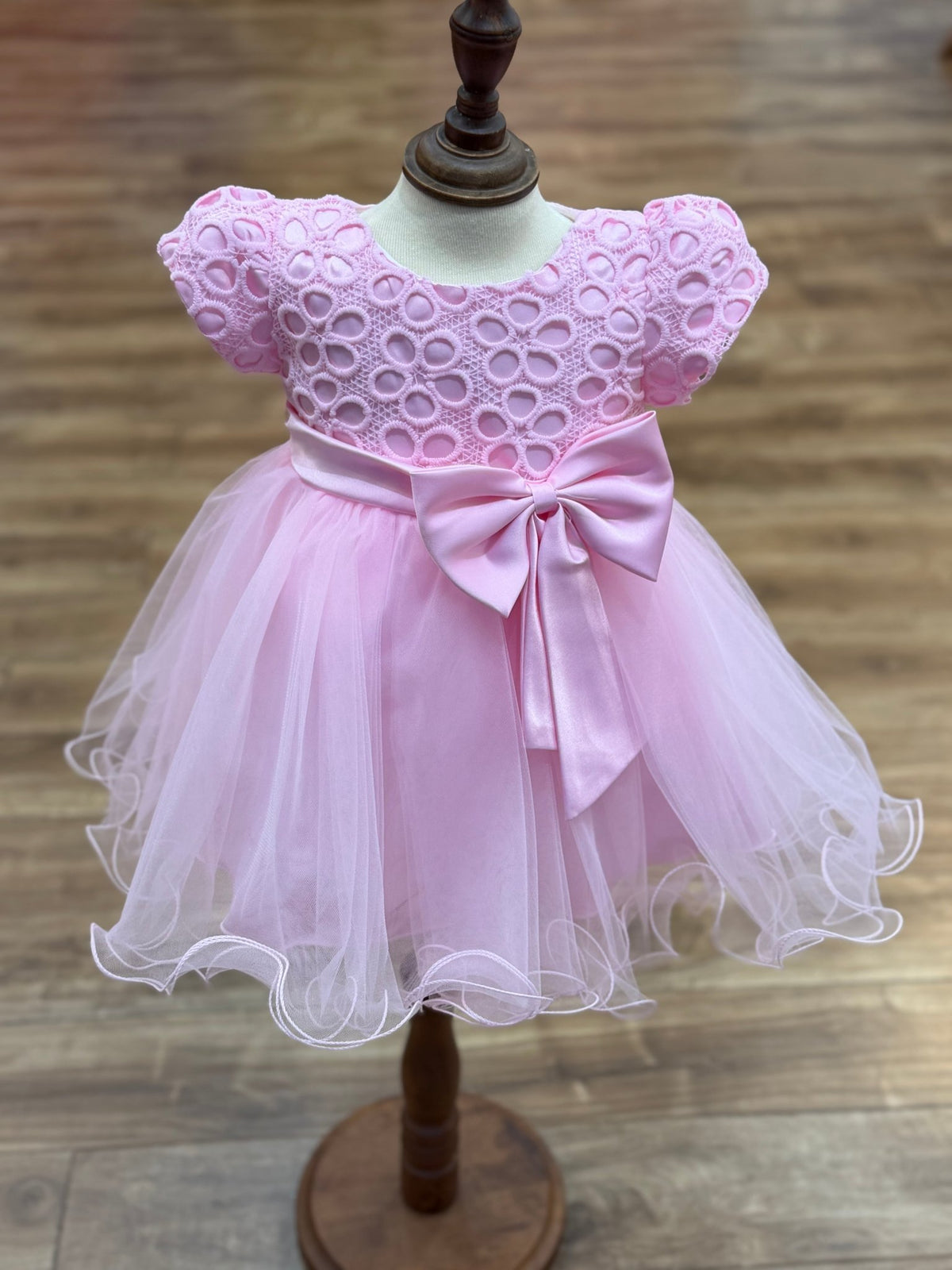 Pink flower girl dress front view with layered skirt and oversized bow detail.