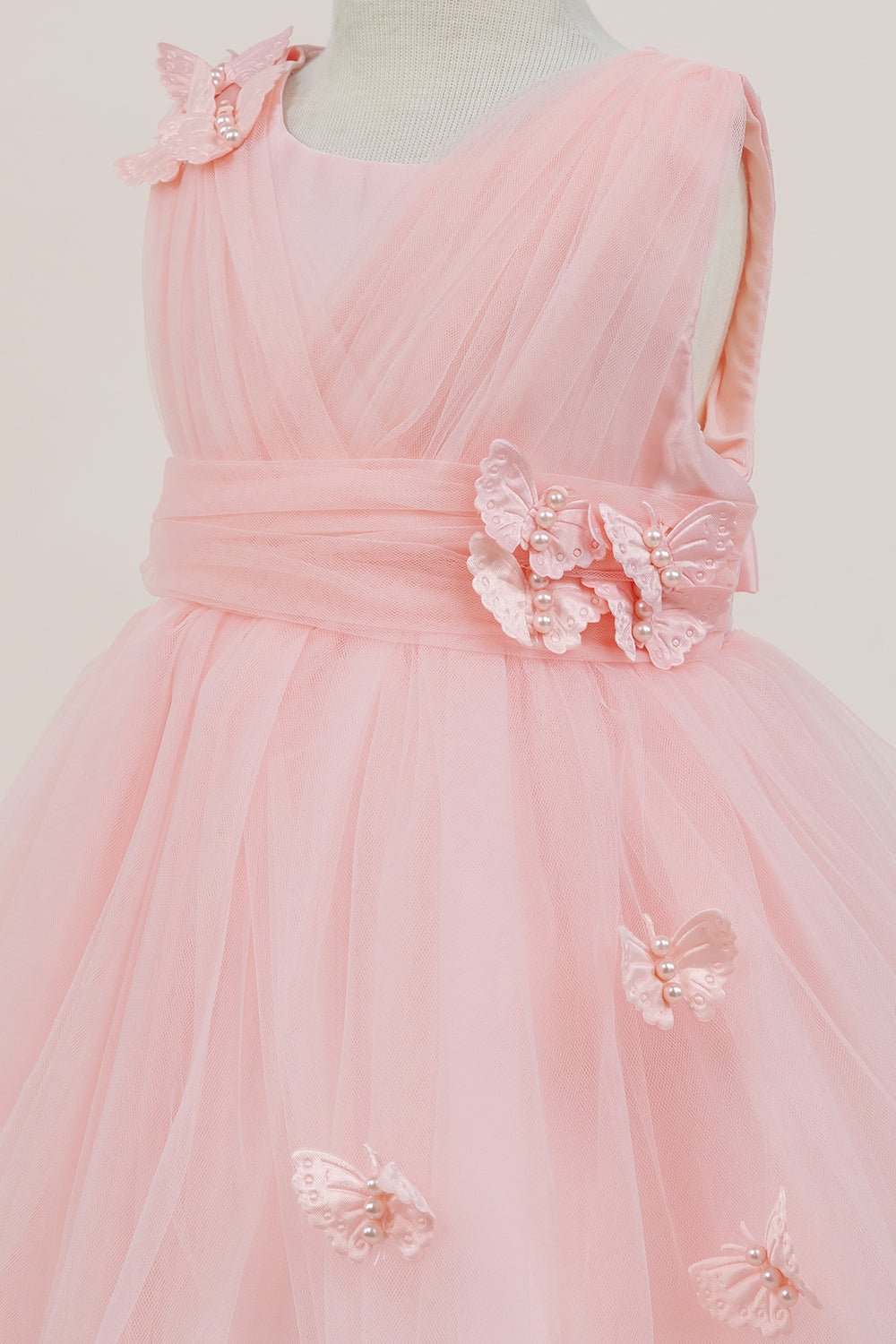 Close-up front view of peach flower girl dress showing shimmering fabric and bow accent.