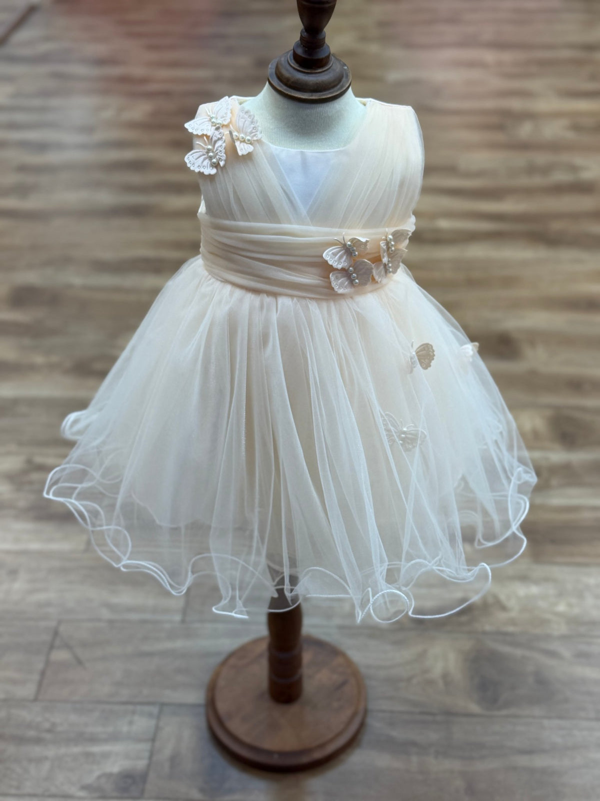 Champagne flower girl dress front view with layered skirt and oversized bow detail.