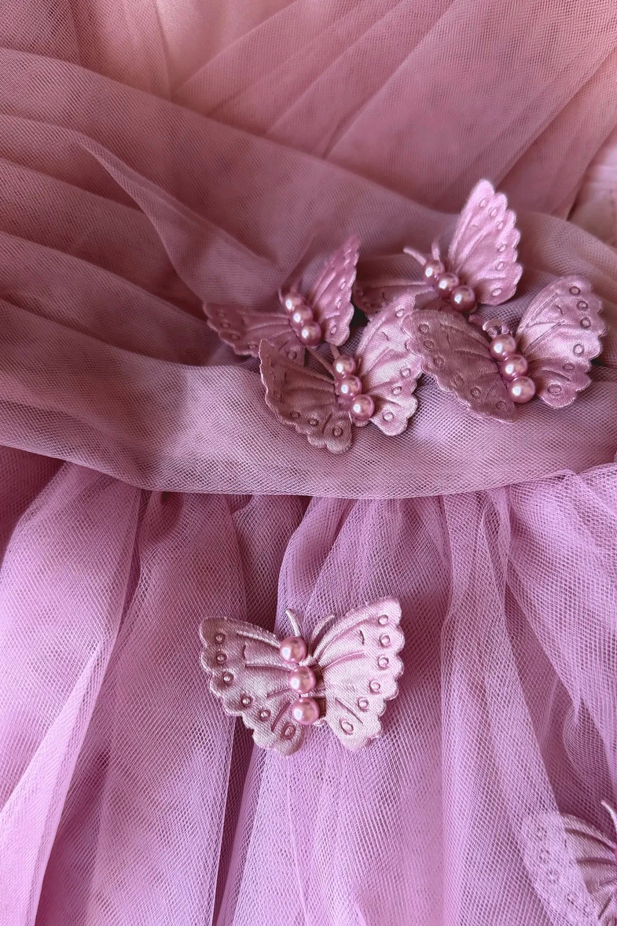 A close-up of rose tulle dress, decorated with six pink butterfly appliqués embellished with small pearls.