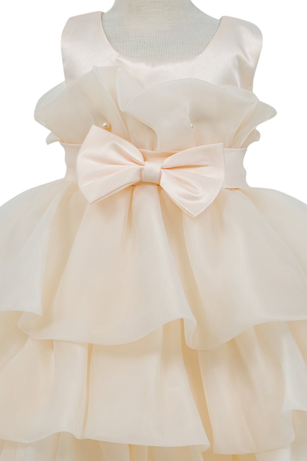 Close-up front view of champagne flower girl dress showing shimmering fabric and bow accent.