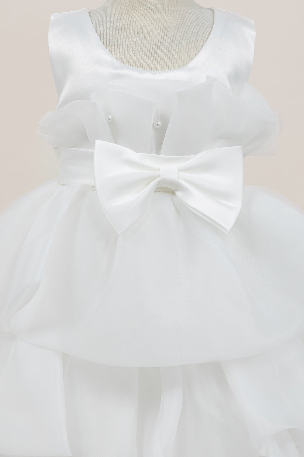 Close-up front view of white flower girl dress showing shimmering fabric and bow accent.