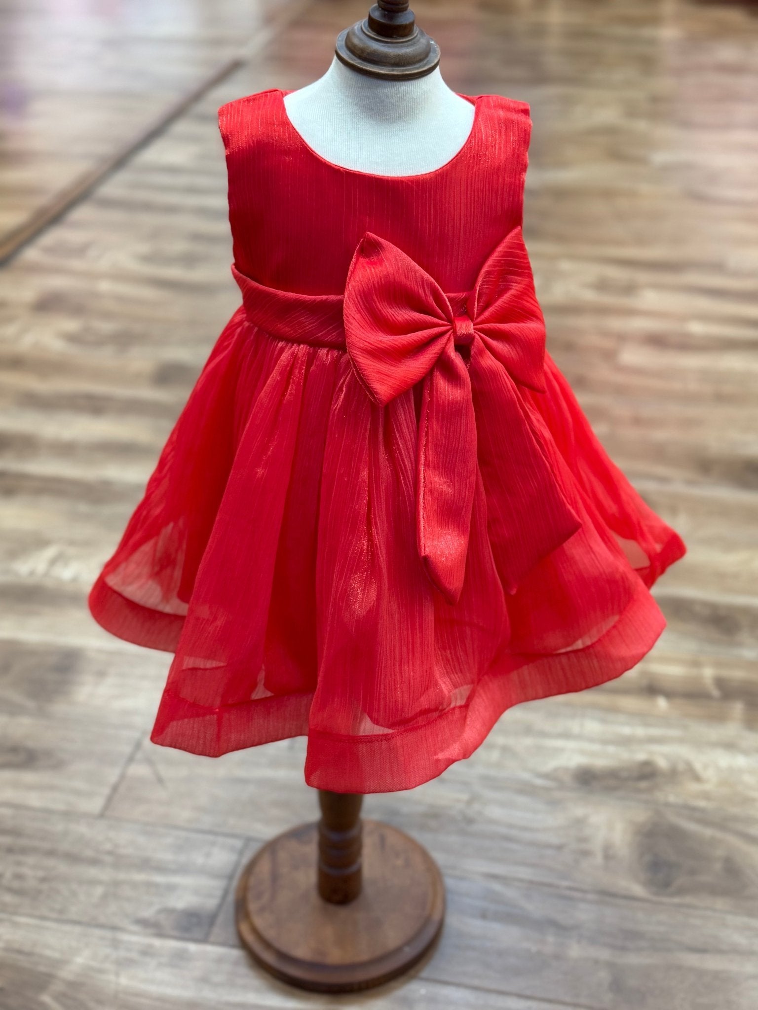 Red flower girl dress front view with layered skirt and oversized bow detail.