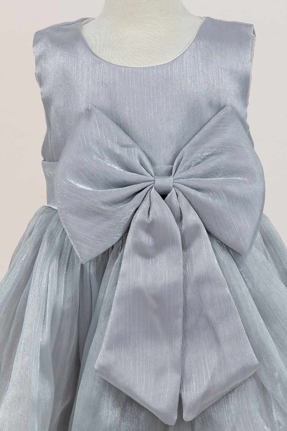 Close-up front view of silver flower girl dress showing shimmering fabric and bow accent.