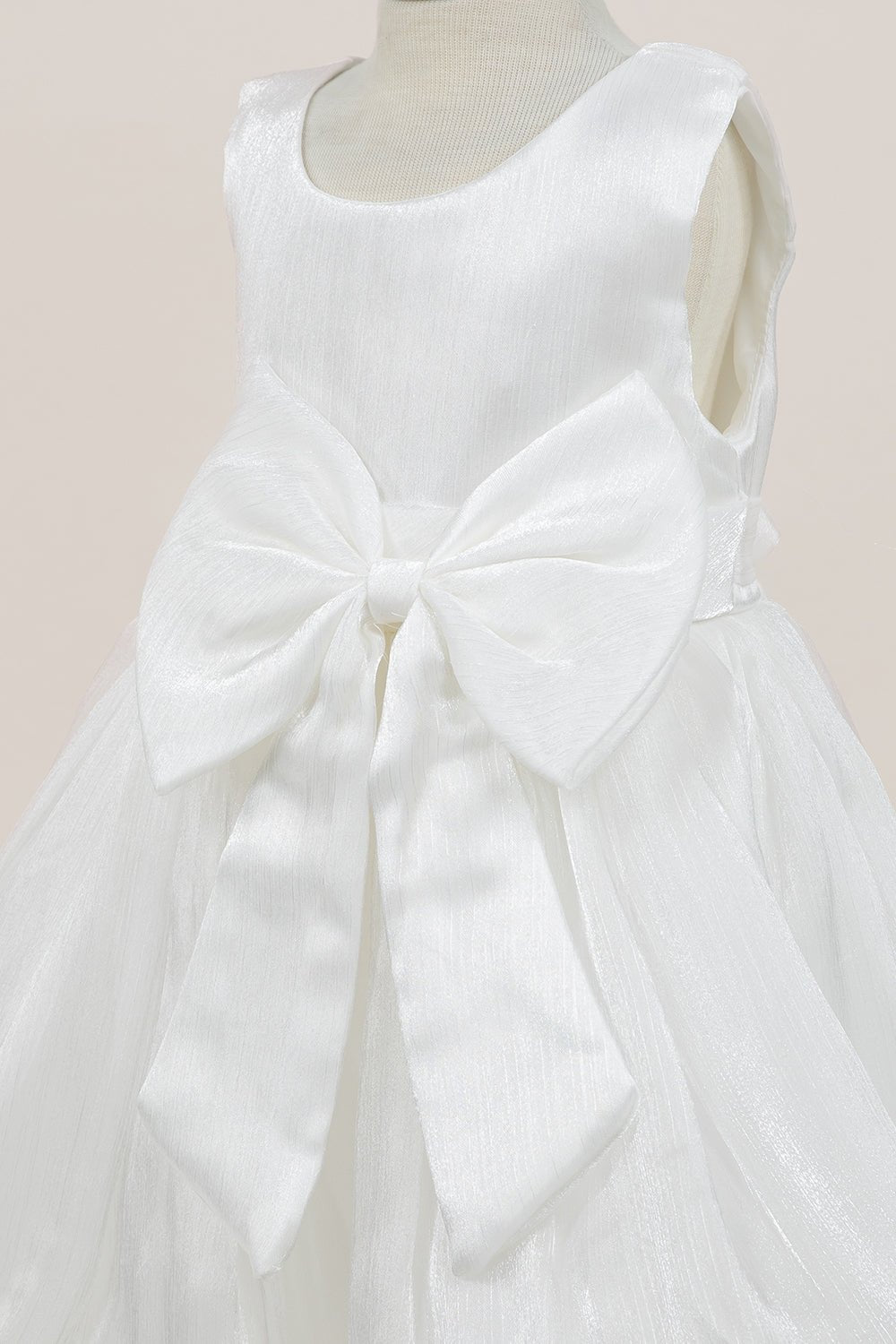 Close-up front view of white flower girl dress showing shimmering fabric and bow accent.