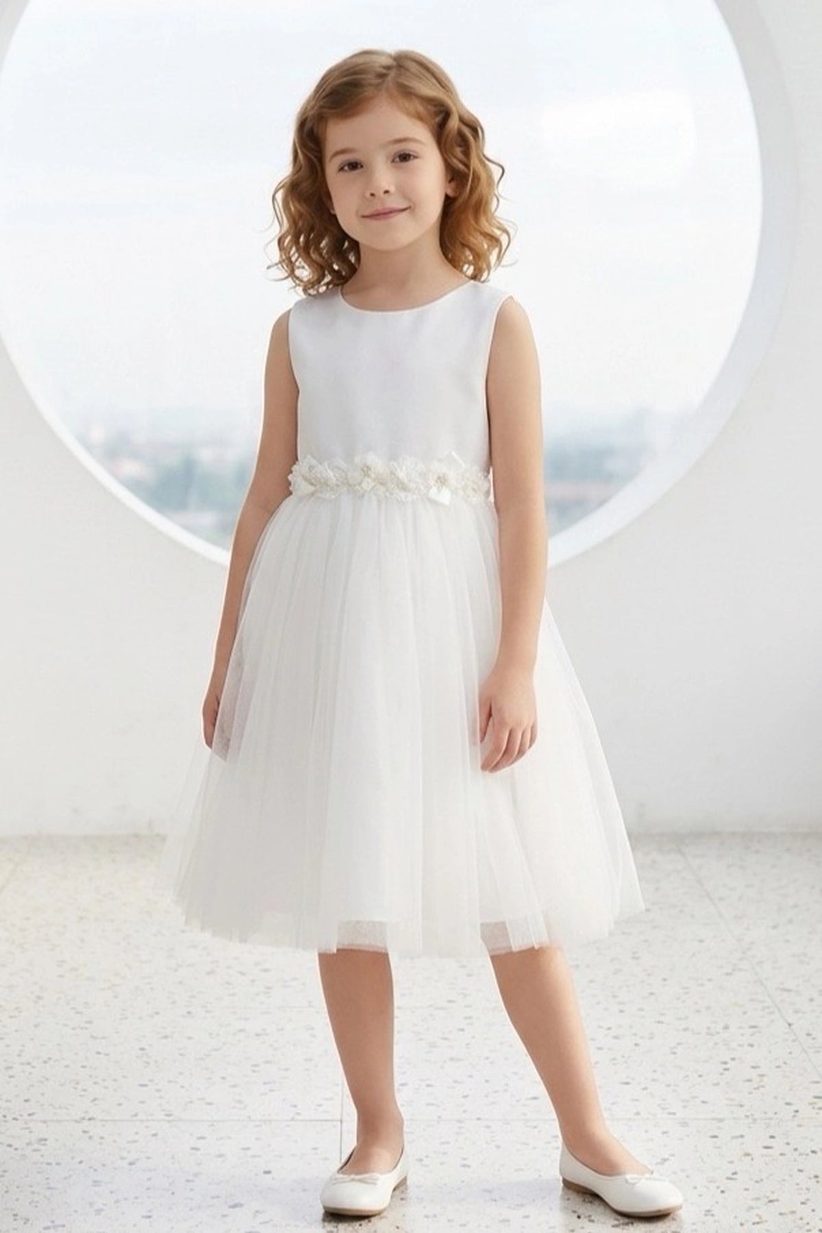 White flower girl dress features floral waistband above a full tulle skirt.