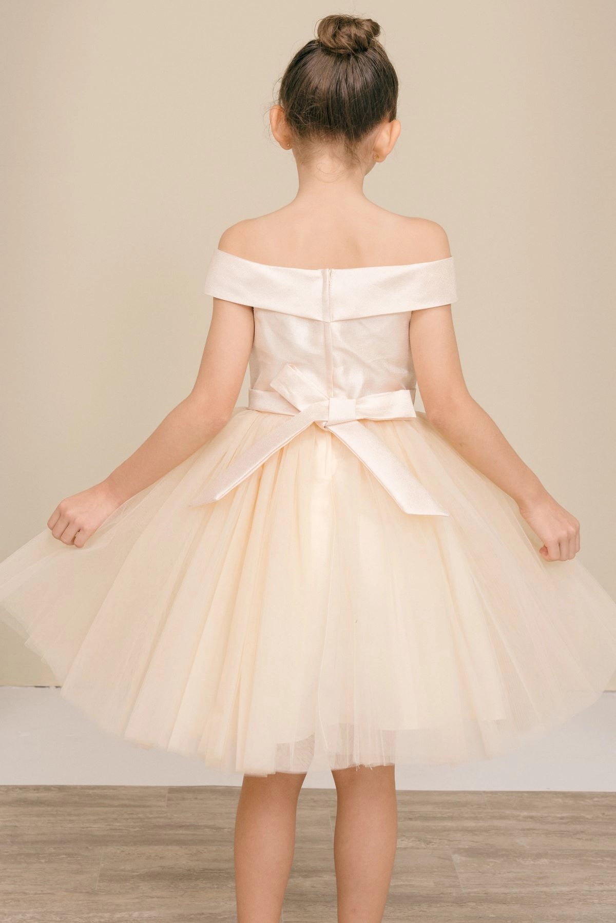 A Champagne flower girl dress showing back bow and zipper below the satin band.