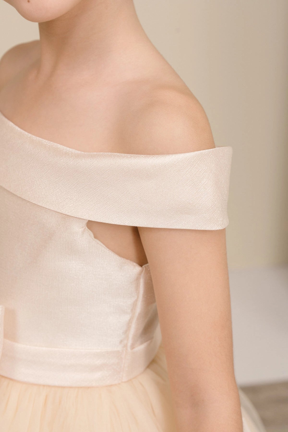 Details of the Champagne flower girl dress include folded satin band around the off-shoulder neckline.