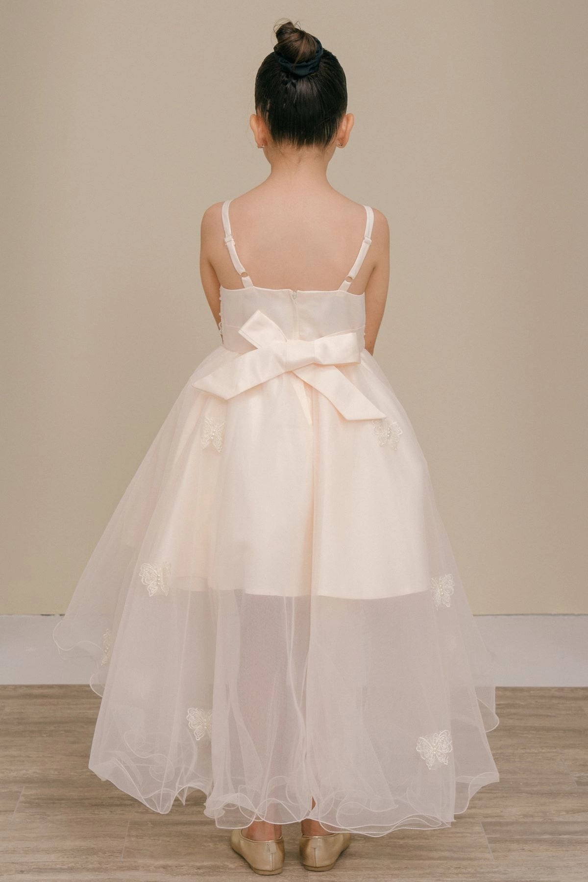 Finished details of a large bow above a high-low skirt distinguish the Champagne kids party dress.