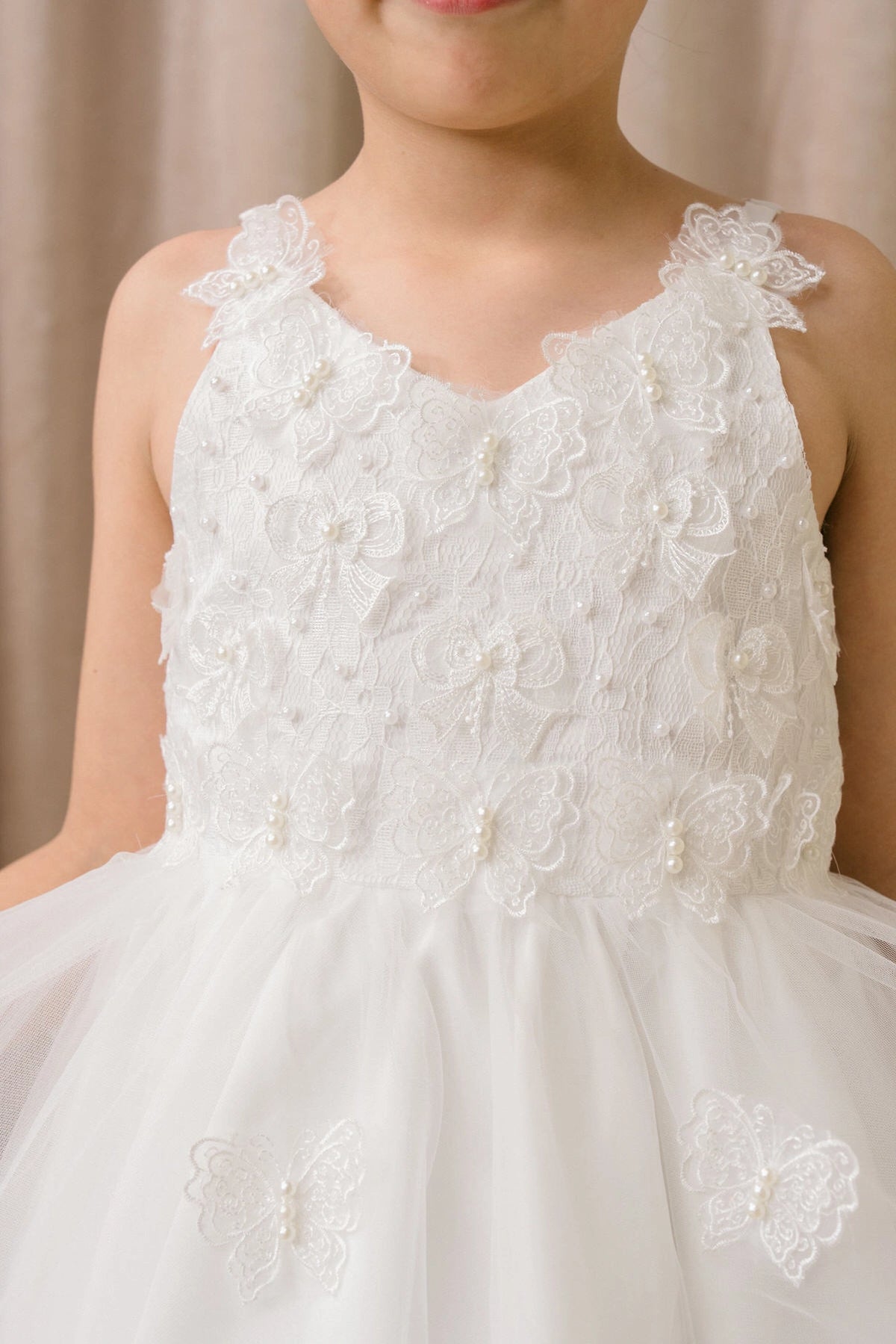 Detailed by a tiered high-low skirt, the White kids party dress reveals its construction.