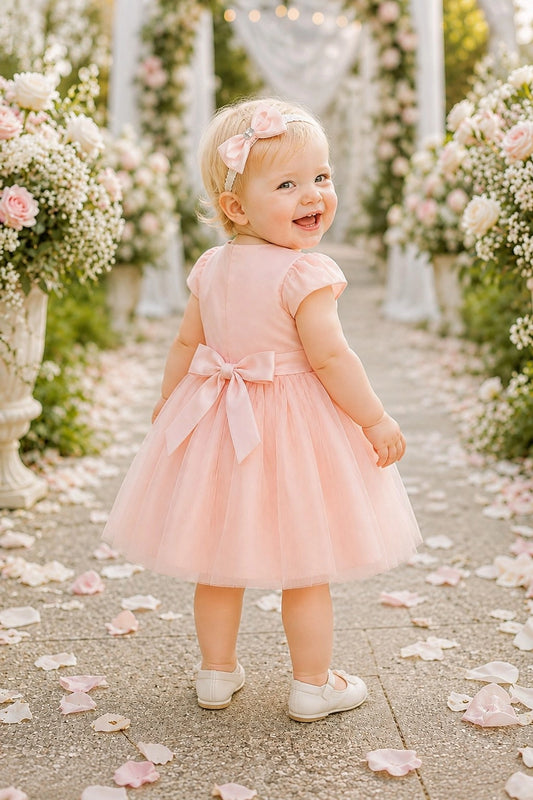 Tied at the back, the Blush kids dress features a large bow.