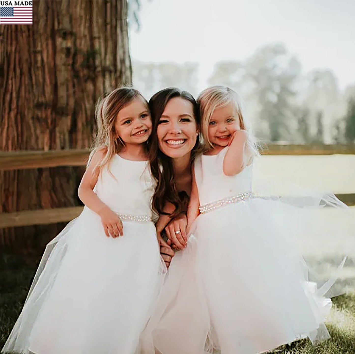 Woman with two young girls in white dresses sitting outdoors.