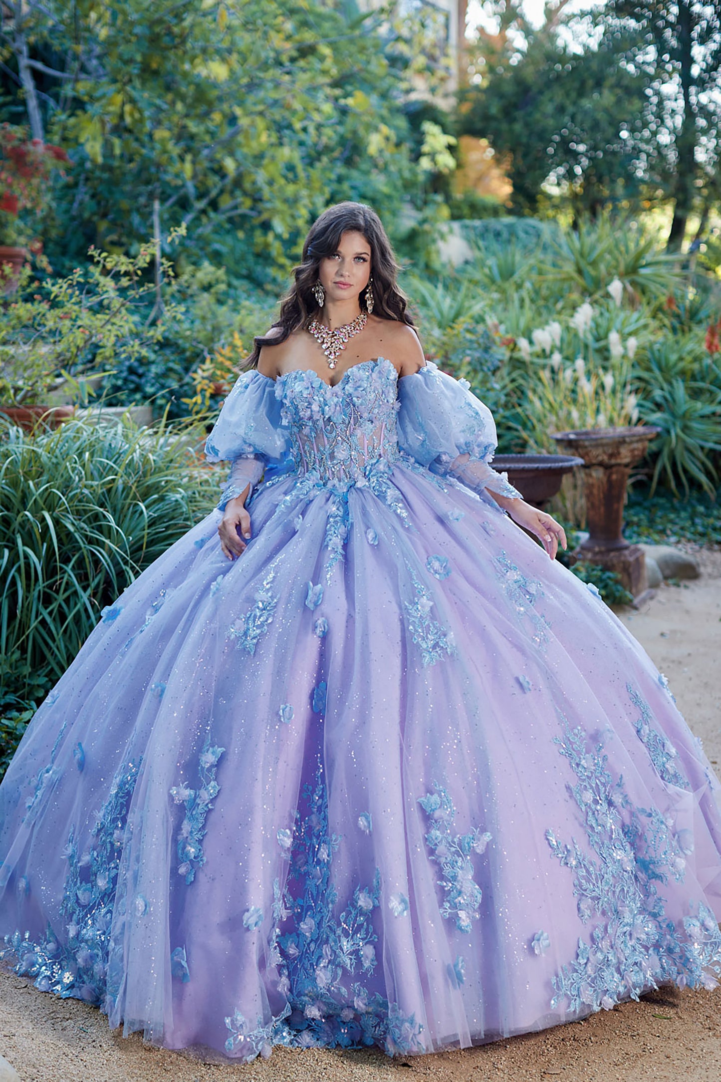 Quinceanera | Detachable Puff Sleeves and Cape Sparkly Ball Gown | Lilac Two Tone 3D Floral Detail Quince Dress - front view of woman wearing dress looking into the camera