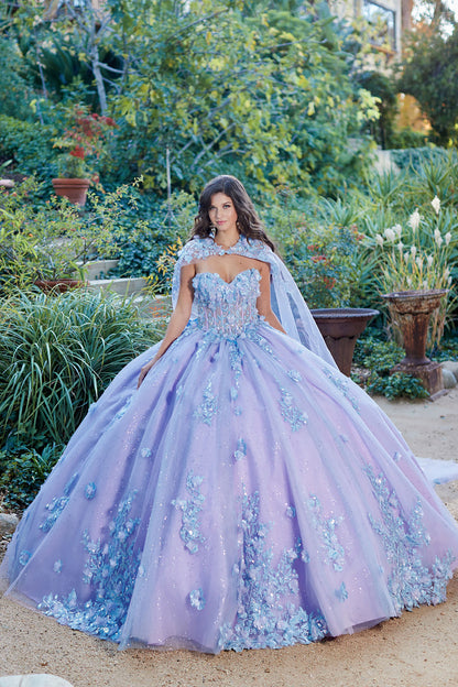 Quinceanera | Detachable Puff Sleeves and Cape Sparkly Ball Gown | Lilac Two Tone 3D Floral Detail Quince Dress - front view of woman wearing dress looking directly into the camera standing in front of plants