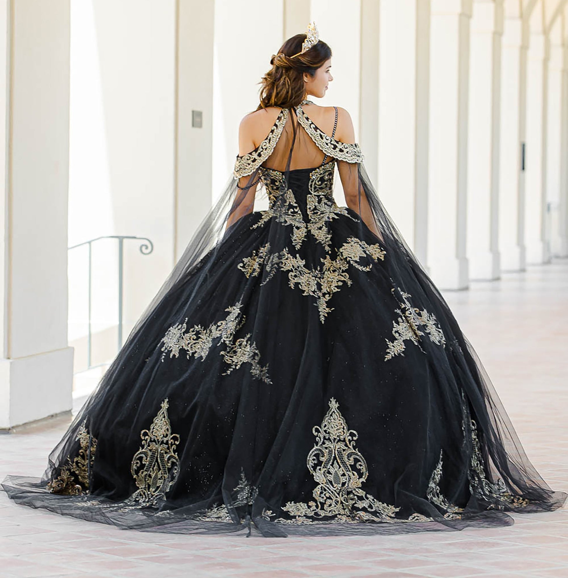 Quinceanera | Black with Gold Embroidered Lace with Stunning Cape Quince Ballgown dress - back view of woman wearing dress standing in front of pillars