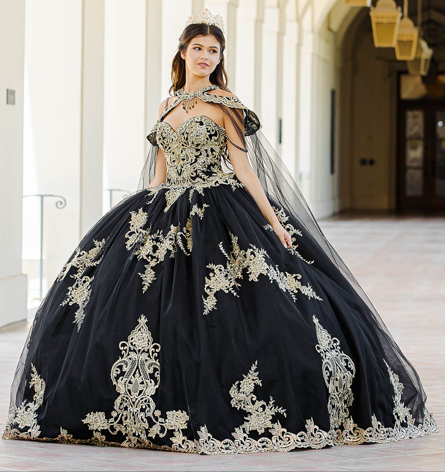 Quinceanera | Black with Gold Embroidered Lace with Stunning Cape Quince Ballgown dress - front view of woman wearing dress and staring of into the distance