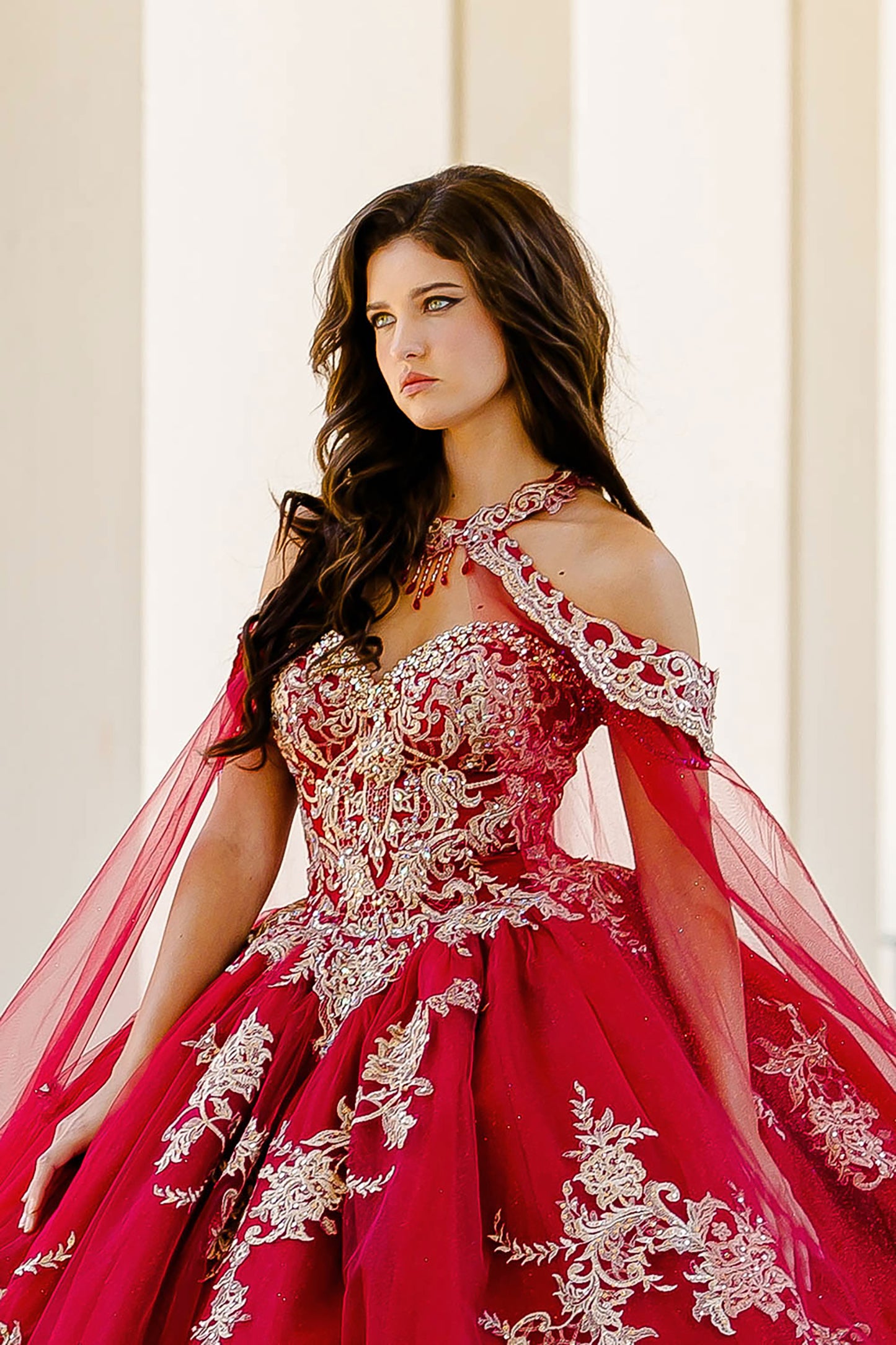 Quinceanera | Wine with Gold Embroidered Lace with Stunning Cape Quince Ballgown dress - front view of woman wearing dress staring off into the distance