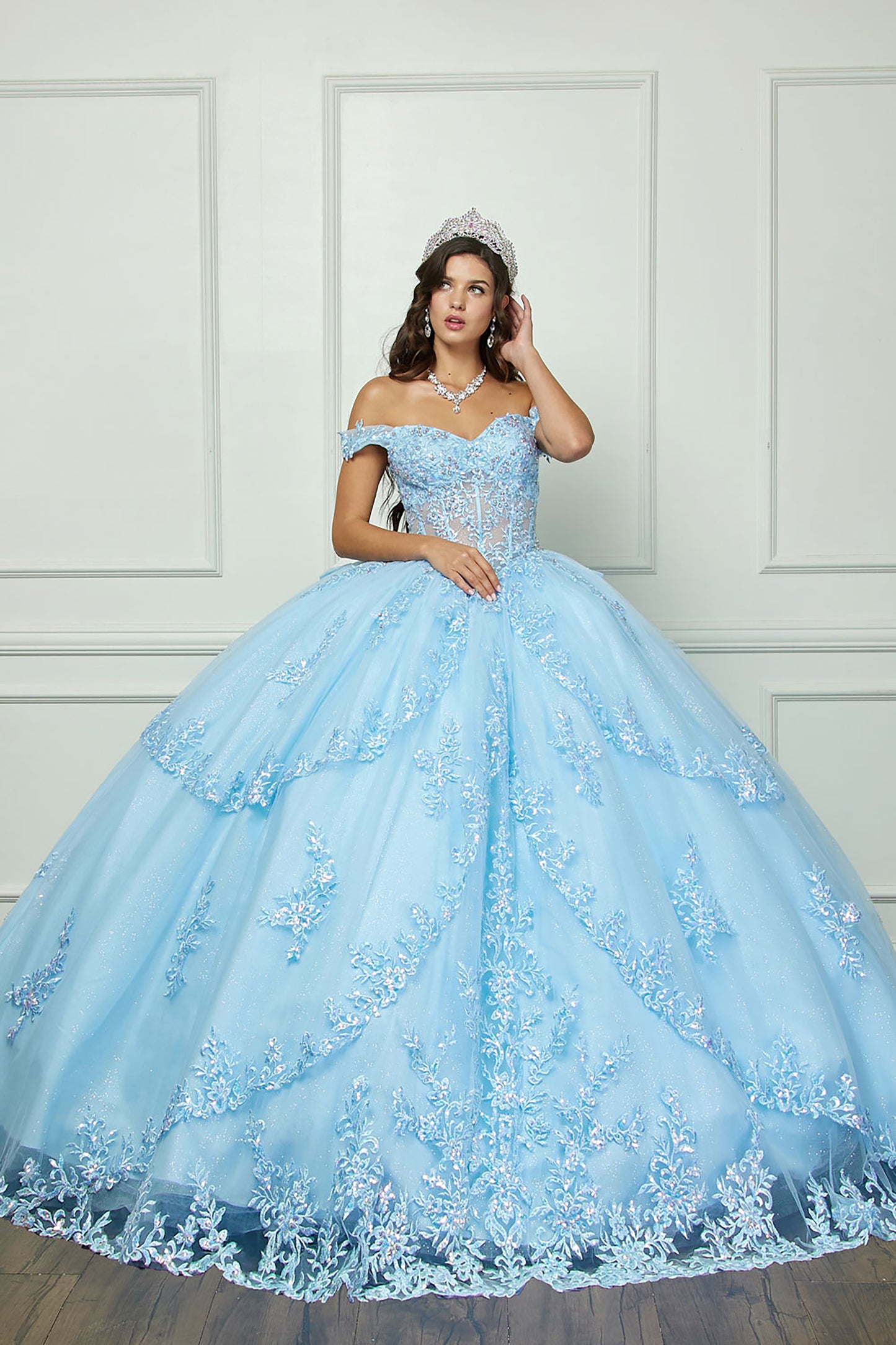 Quinceanera | Cinderella Blue Sparkling Rhinestones Bodice Multi-tiered Illusion Skirt Embroidery Off Shoulder Quince dress - front view of woman wearing dress and crown with hand at front of dress