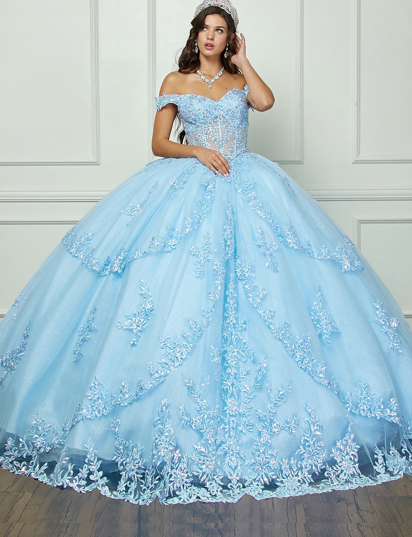 Quinceanera | Cinderella Blue Sparkling Rhinestones Bodice Multi-tiered Illusion Skirt Embroidery Off Shoulder Quince dress - front view of woman wearing dress and crown with hand at front of dress