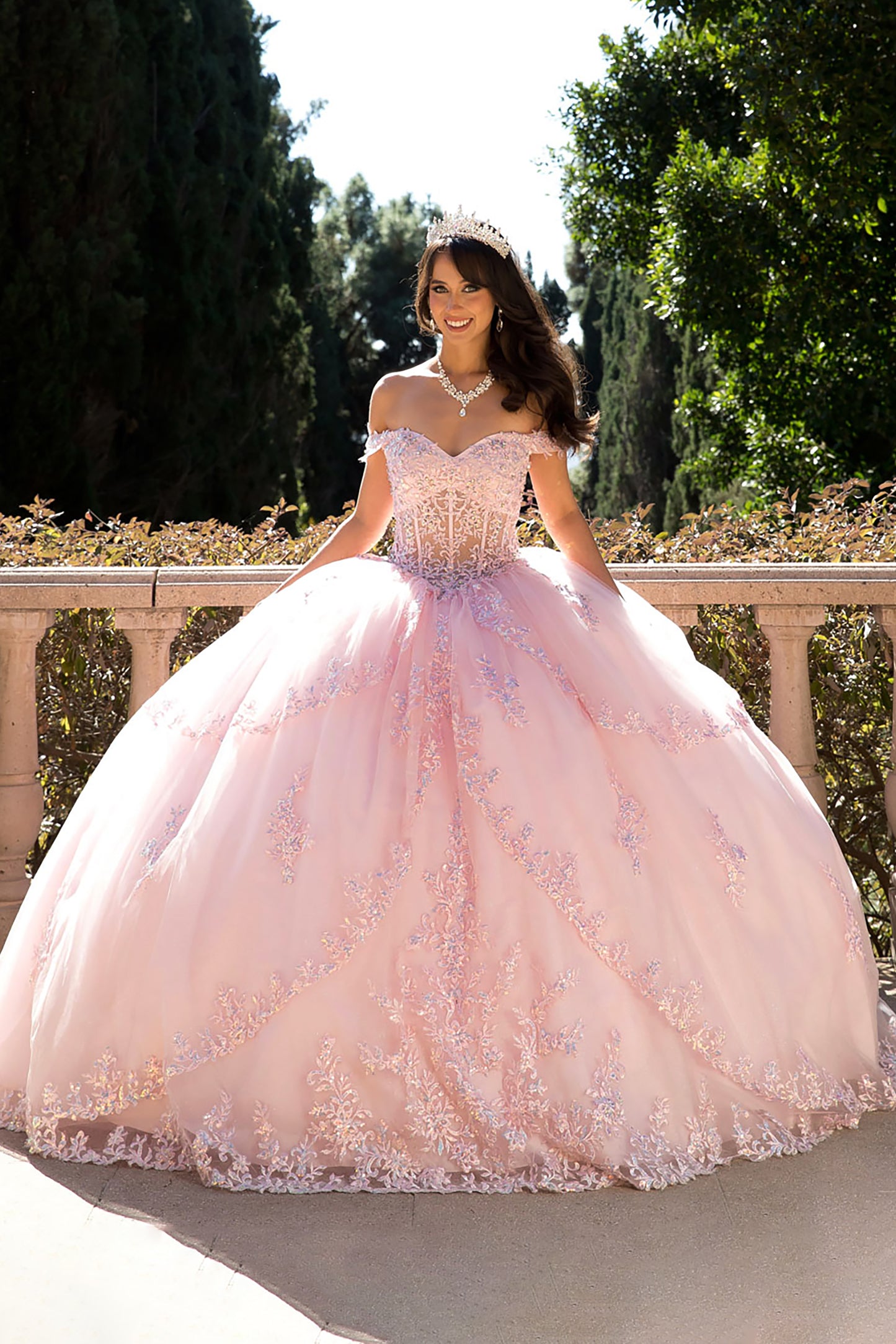 Girl in a pink quinceañera dress standing outdoors with greenery in the background