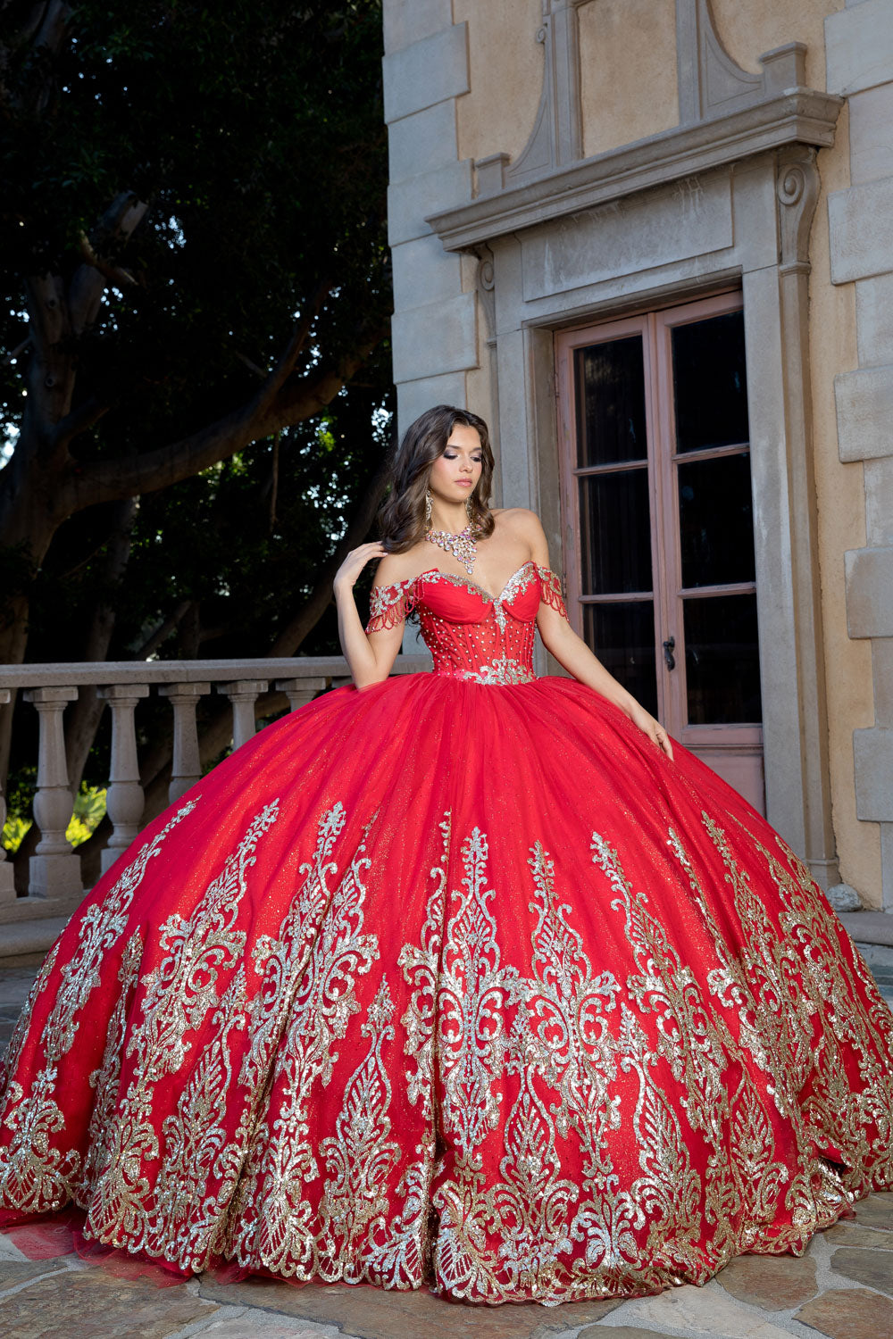Woman in a red and gold ball gown standing in front of a stone building.