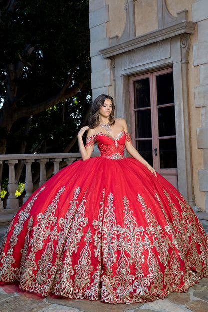 Woman in a red and gold ball gown standing in front of a stone building.