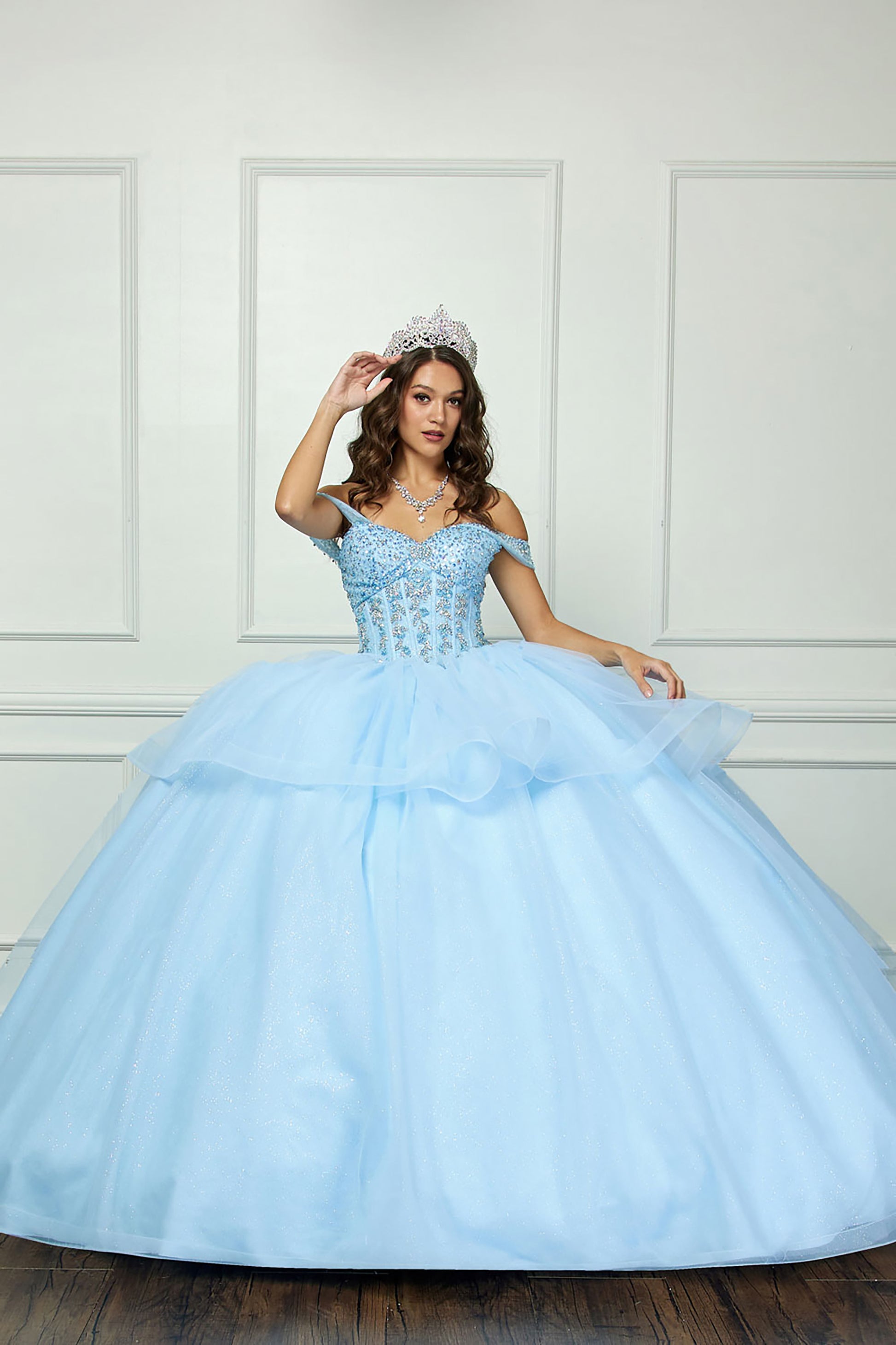 Quinceañera | Blue Glittering Tulle Layers, Off-shoulder Bodice adornments, and a detachable bow - front view of woman wearing dress with one hand near crown