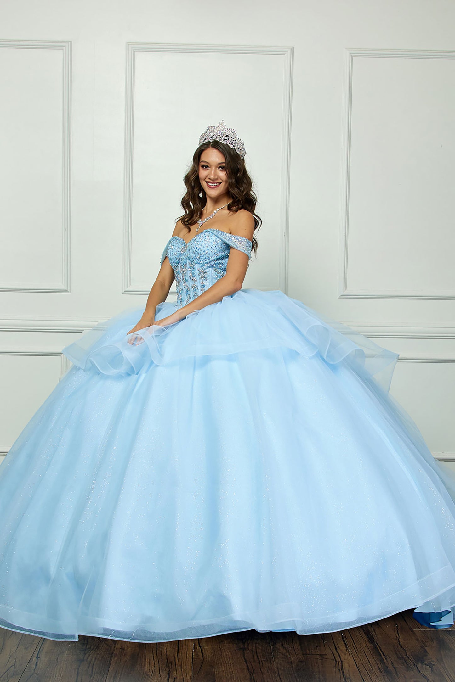 Quinceañera | Blue Glittering Tulle Layers, Off-shoulder Bodice adornments, and a detachable bow - side view of woman wearing dress and smiling