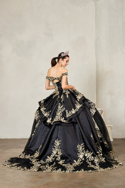 Woman in a black and gold quince gown with floral embroidery against a plain background