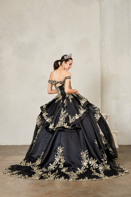 Woman in a black and gold quince gown with floral embroidery against a plain background