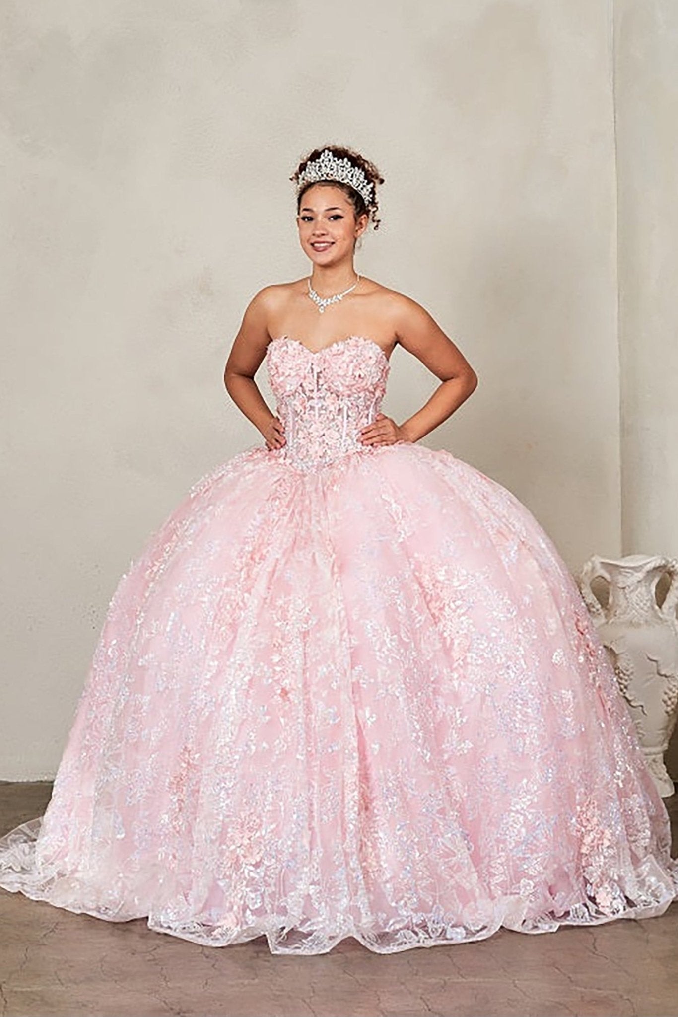 Woman in a pink ball gown with floral and butterfly details against a plain background