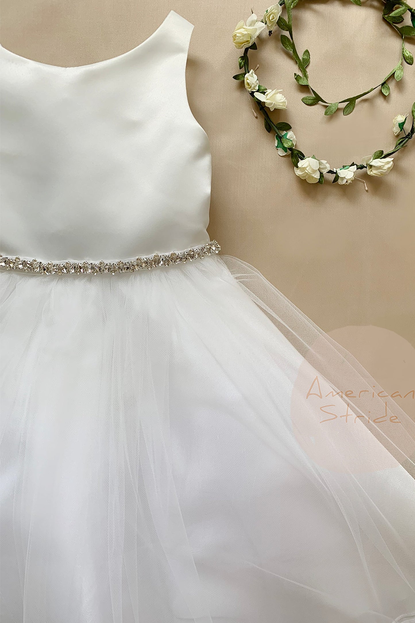 White dress with a sparkling waistband and floral headband on a beige background