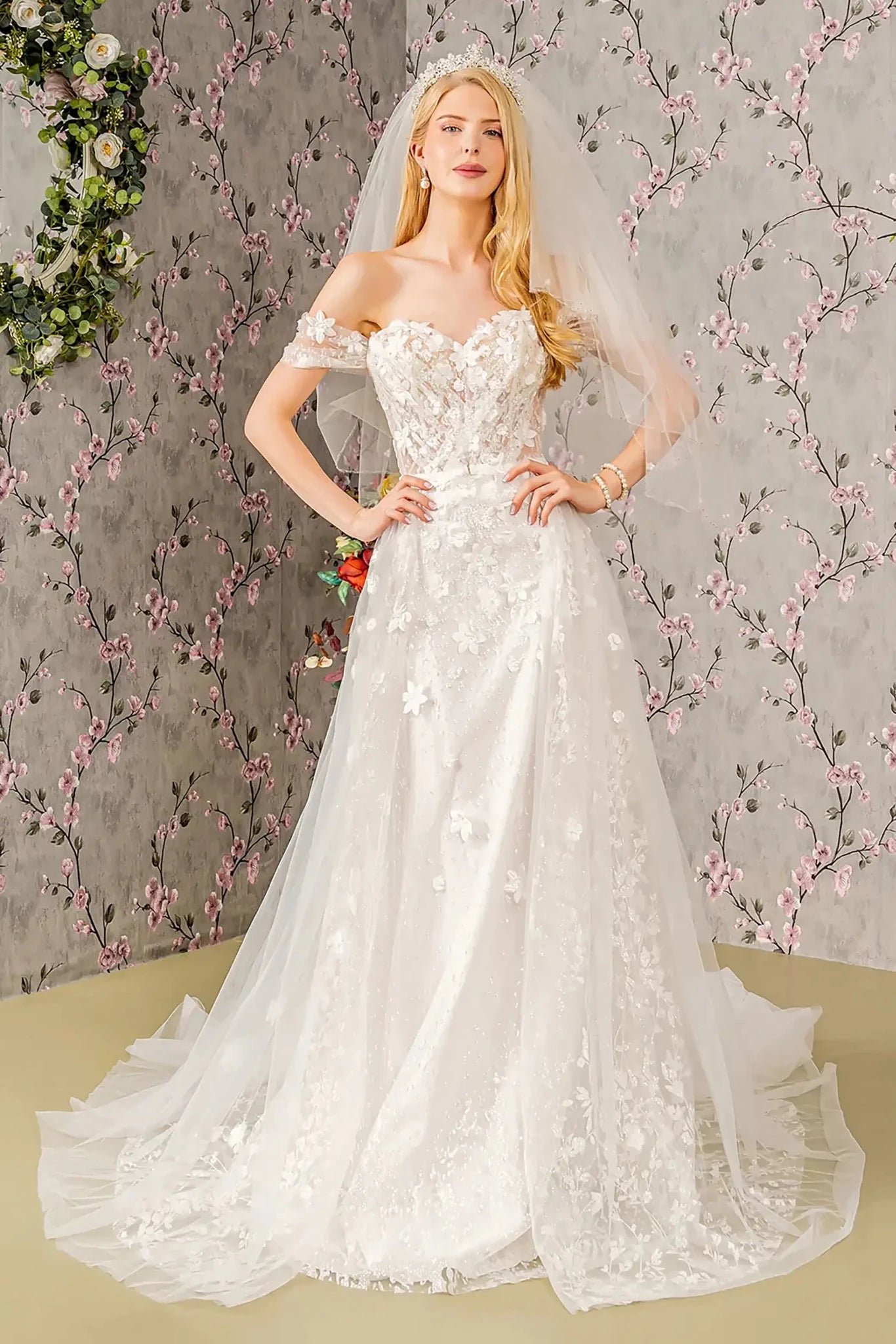Front full-length view of an ivory A-line wedding dress featuring a sweetheart neckline, off-shoulder sheer bodice, and a voluminous skirt shimmering with jeweled glitter appliqué.